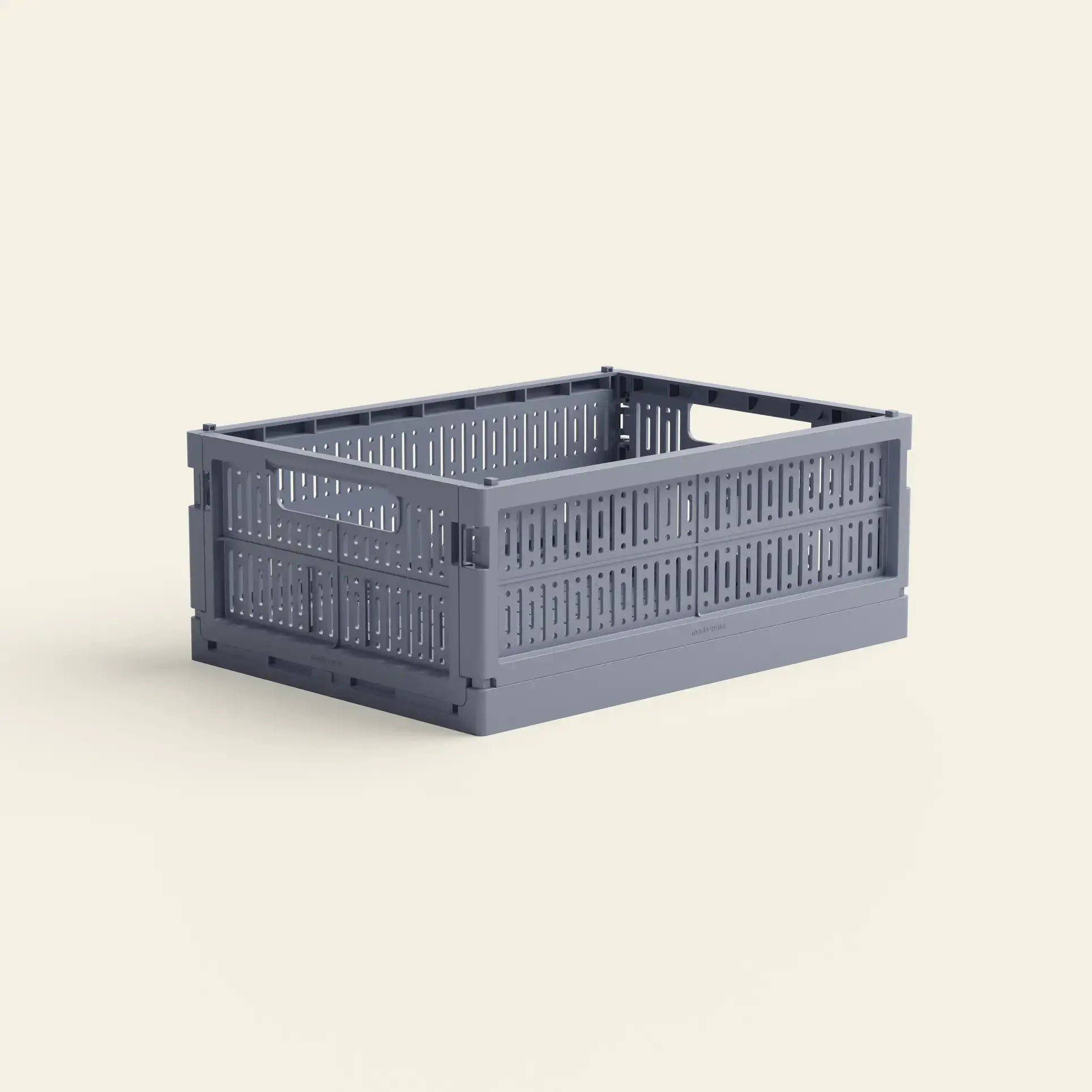 The Made Crate Midi by Made Crate is a lightweight, stackable gray rectangular storage crate made from recycled plastic with perforated sides and handles, shown on a light beige background.