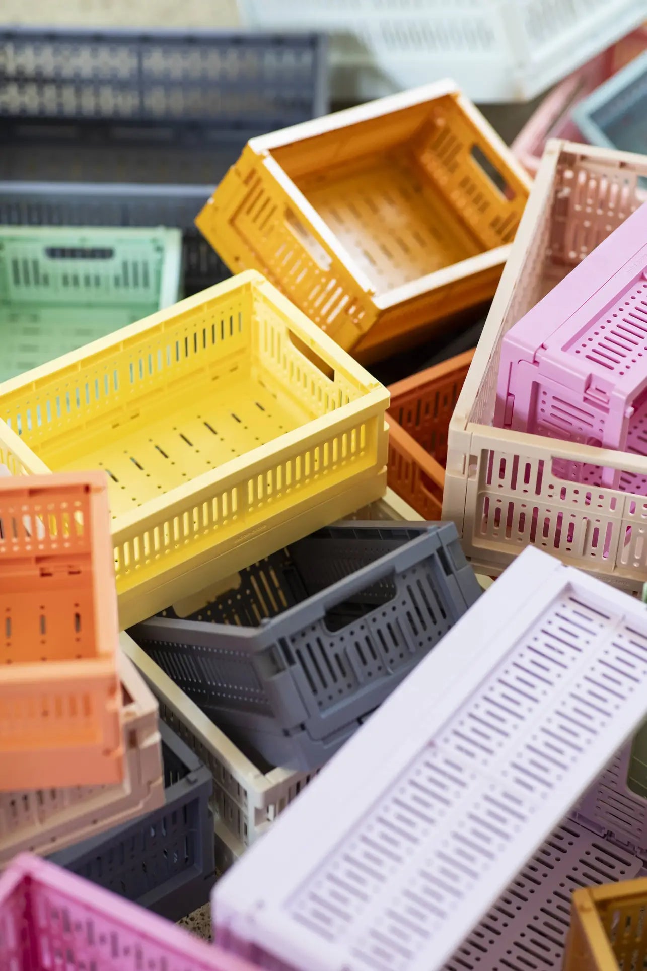 A stack of Made Crate Midi folding crates by Made Crate in eco-friendly recycled plastic, featuring pastel and neutral colors like yellow, orange, black, pink, and beige for convenient storage.