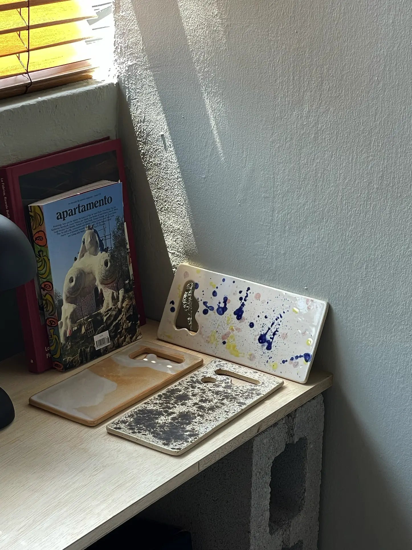 A Mirjam Faber Ceramics Sushi Plate from Mirjam Faber Ceramics rests on a wooden desk near a book titled apartamento and a sunlit window; the desk is supported by cinder blocks.