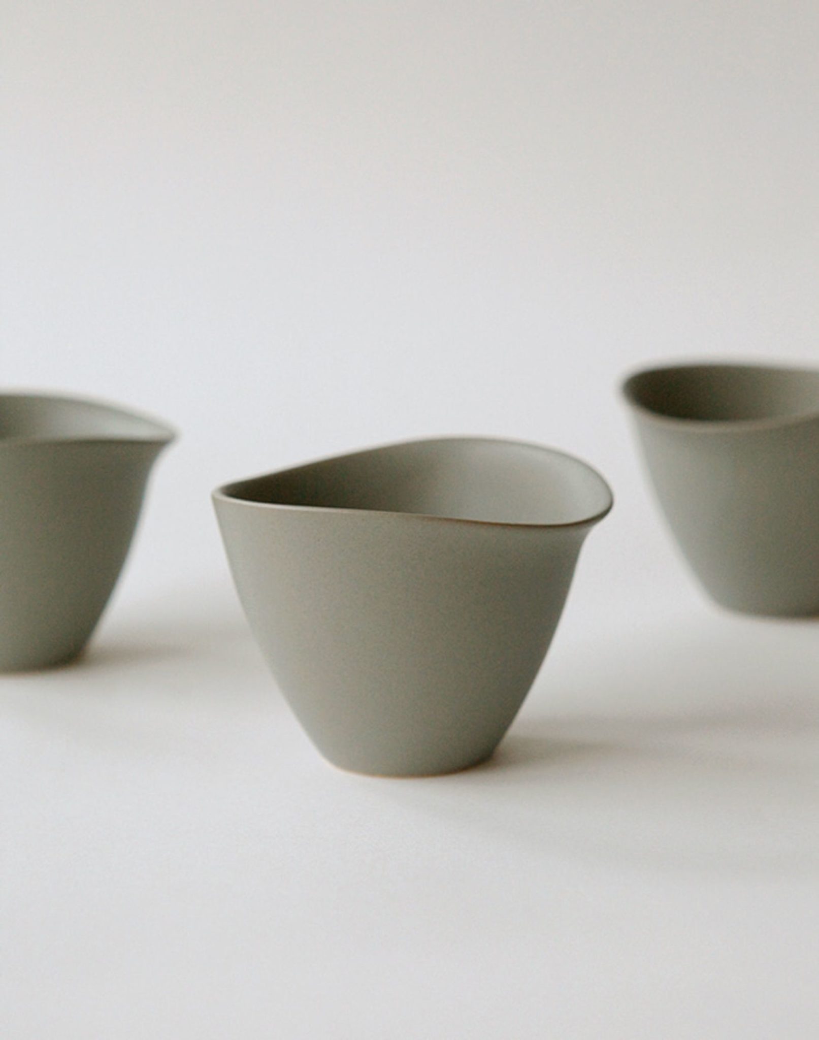 Three NR Ceramics HIN Tea Cups, featuring a minimalist matte grey finish and smooth, organic curves without handles, are elegantly arranged on a plain white background for a modern look.