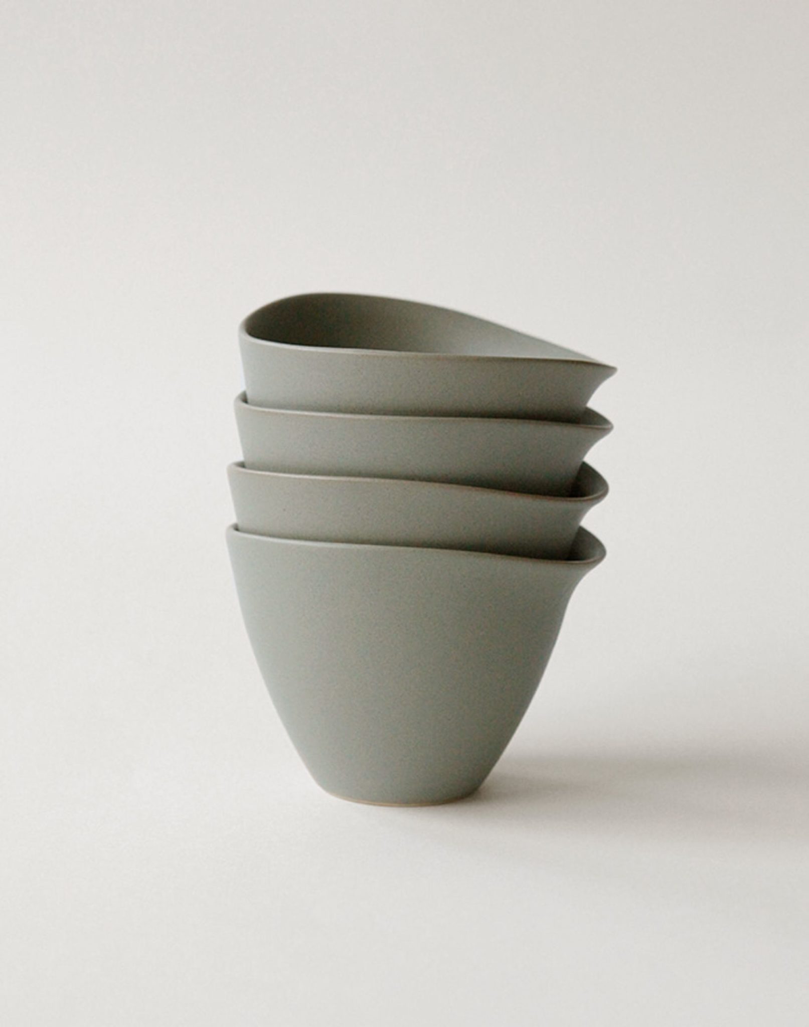 Four NR Ceramics HIN Tea Cups, featuring an ergonomic design with smooth curves and subtle spouts, are stacked neatly on a plain, light background.
