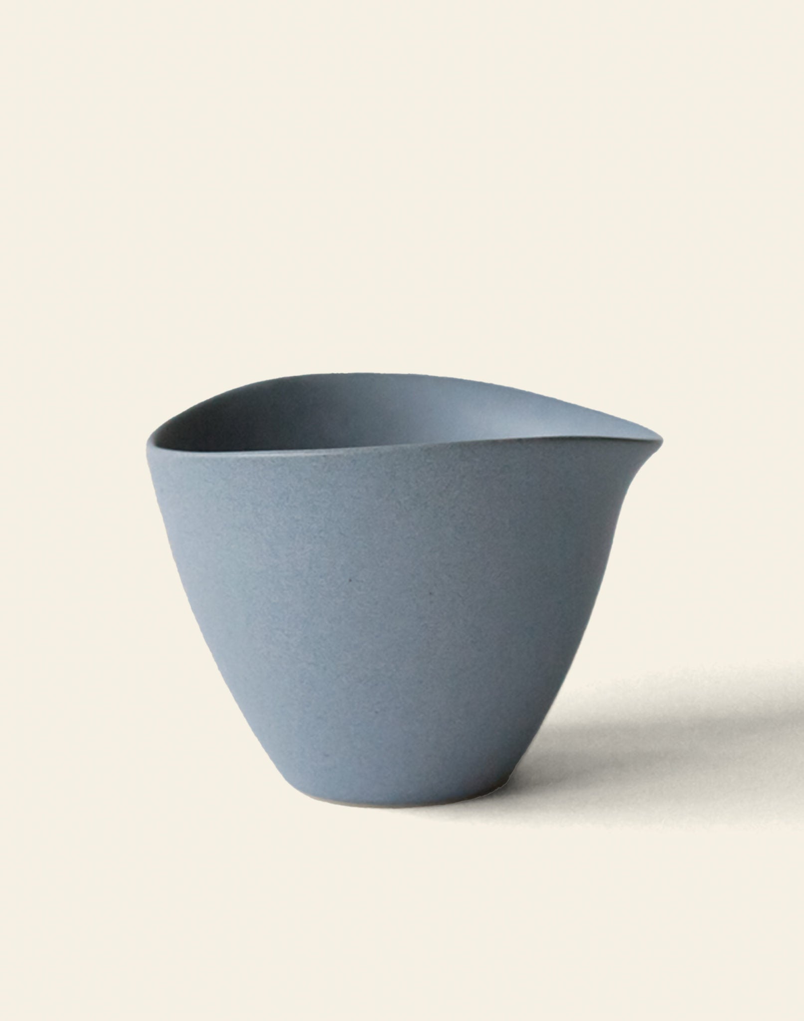The NR Ceramics HIN Tea Cup is a minimalist, matte light blue ceramic cup with an ergonomic design, smooth surface, and asymmetrical pointed rim, shown against a plain off-white background.