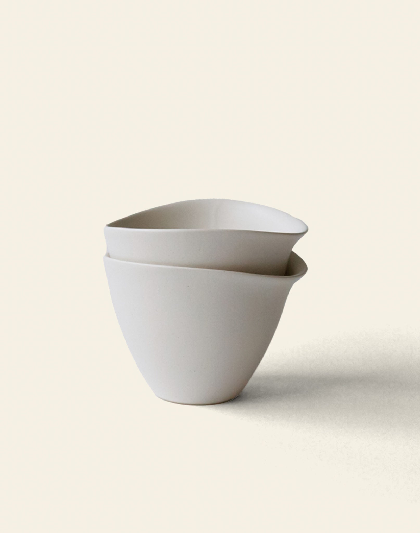 Two minimalist, off-white NR Ceramics HIN Tea Cups are stacked on a light background. Their simple, slightly asymmetrical shape highlights ergonomic design for comfortable daily use.