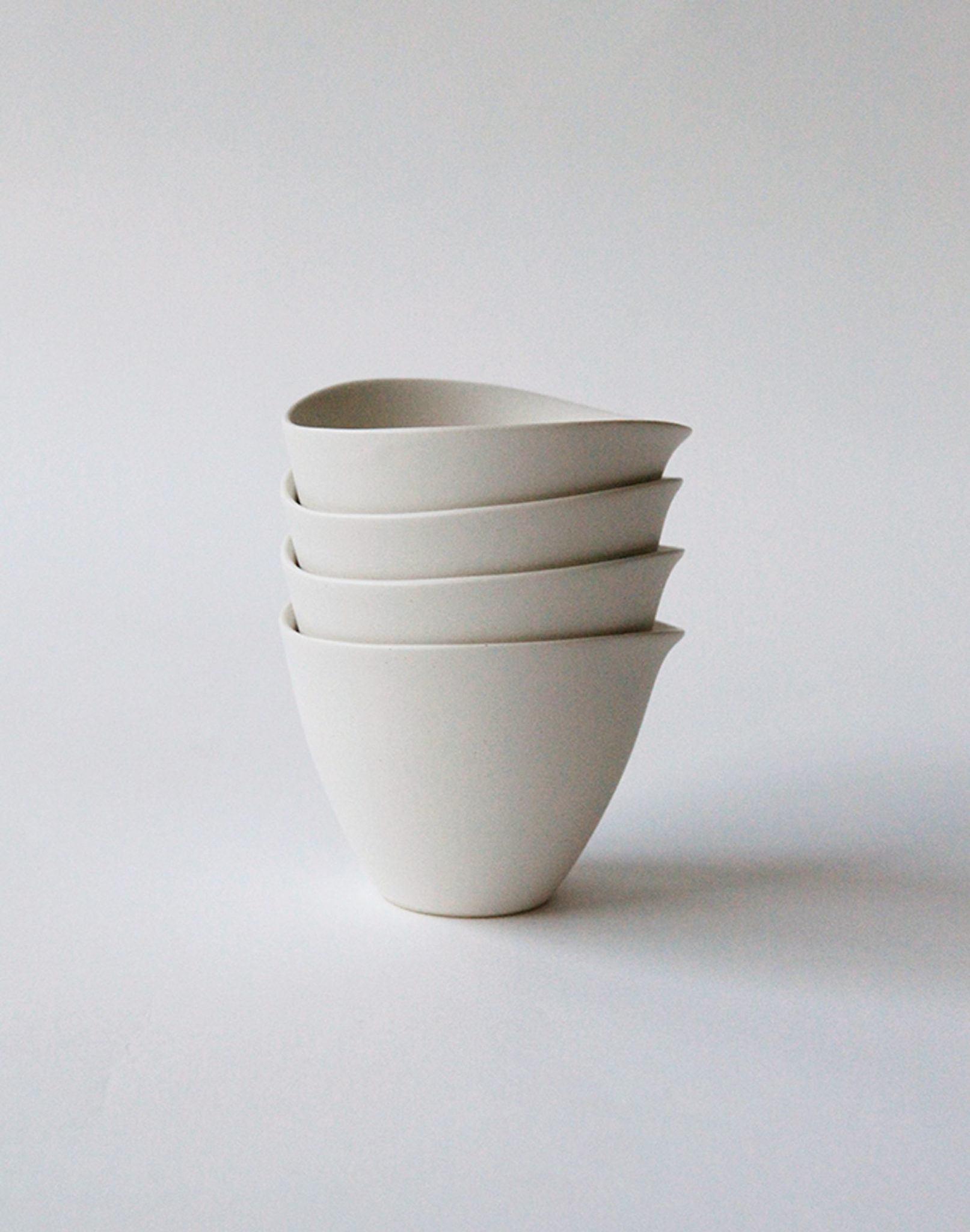 Four white NR Ceramics HIN Tea Cups are stacked neatly against a plain, light background. With a minimalist ergonomic design, smooth surfaces, and a slight spout, these cups by NR Ceramics blend style and functionality.
