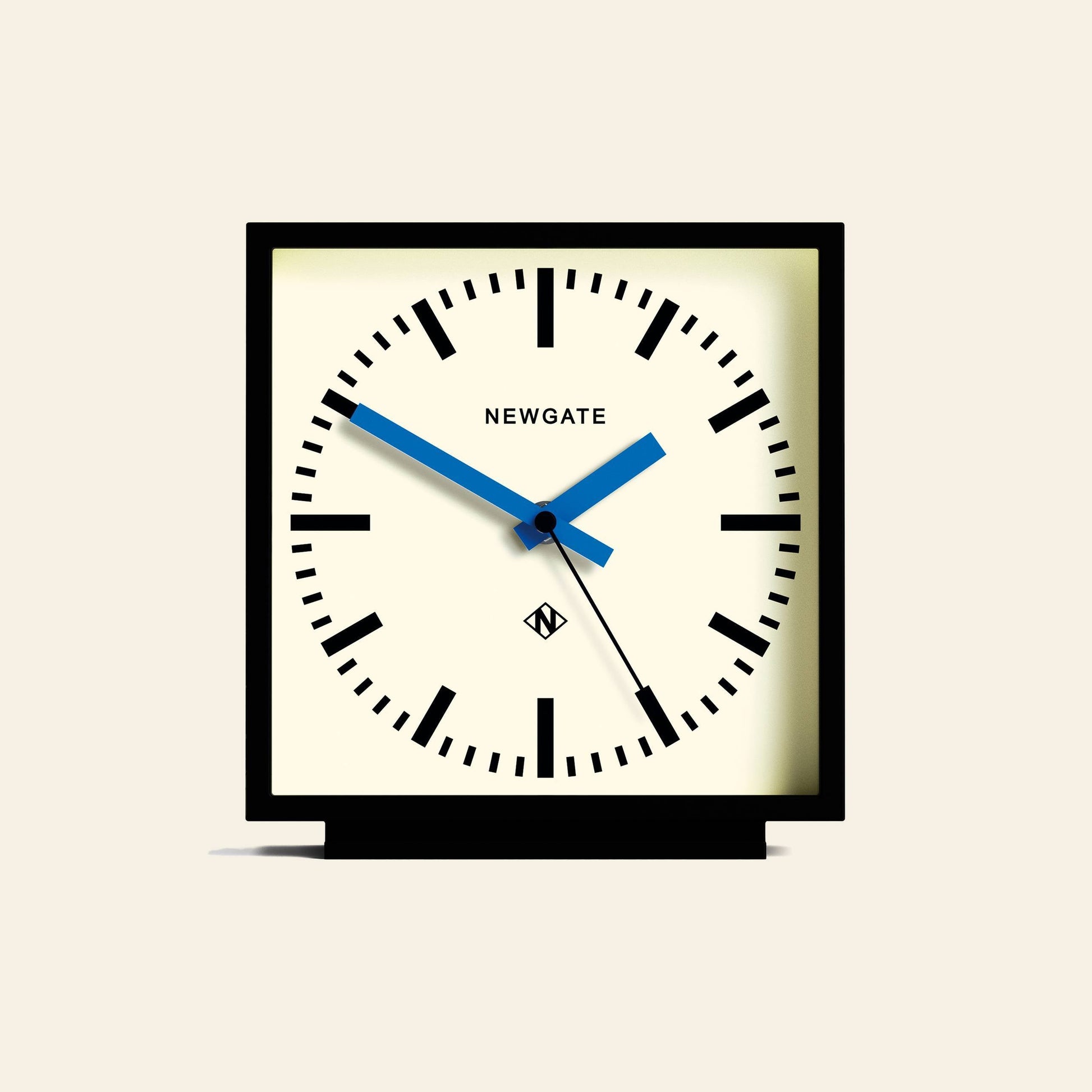The Newgate Amp Mantel Clock features a square black frame, white face, bold black hour markers, and blue hands for classic station style. The Newgate logo appears on the dial, with the clock showing about 10:08.