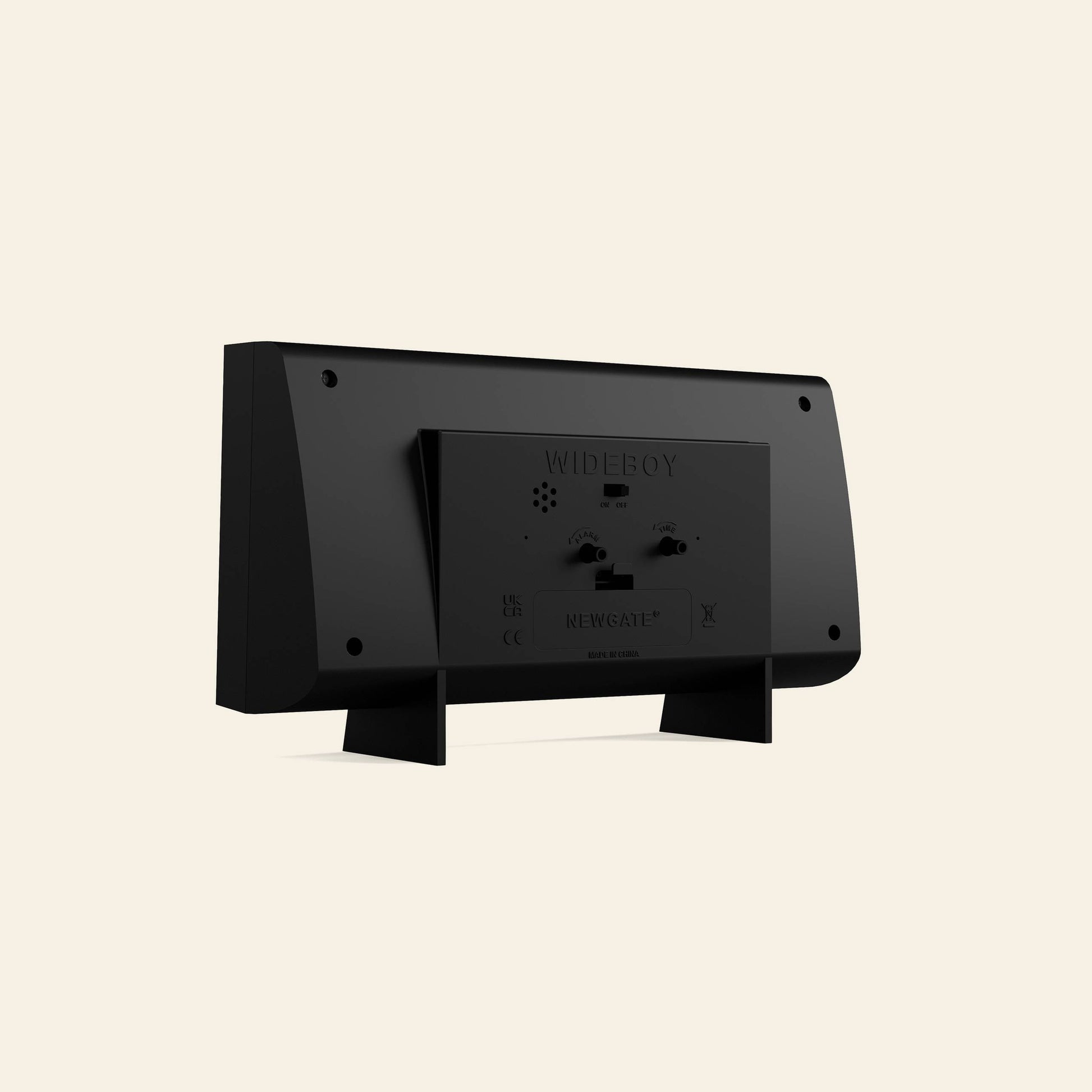 A black Newgate Wideboy Alarm Clock by Newgate, retro-inspired and shown from the back with its stand, battery compartment, and control buttons visible against a plain beige background.
