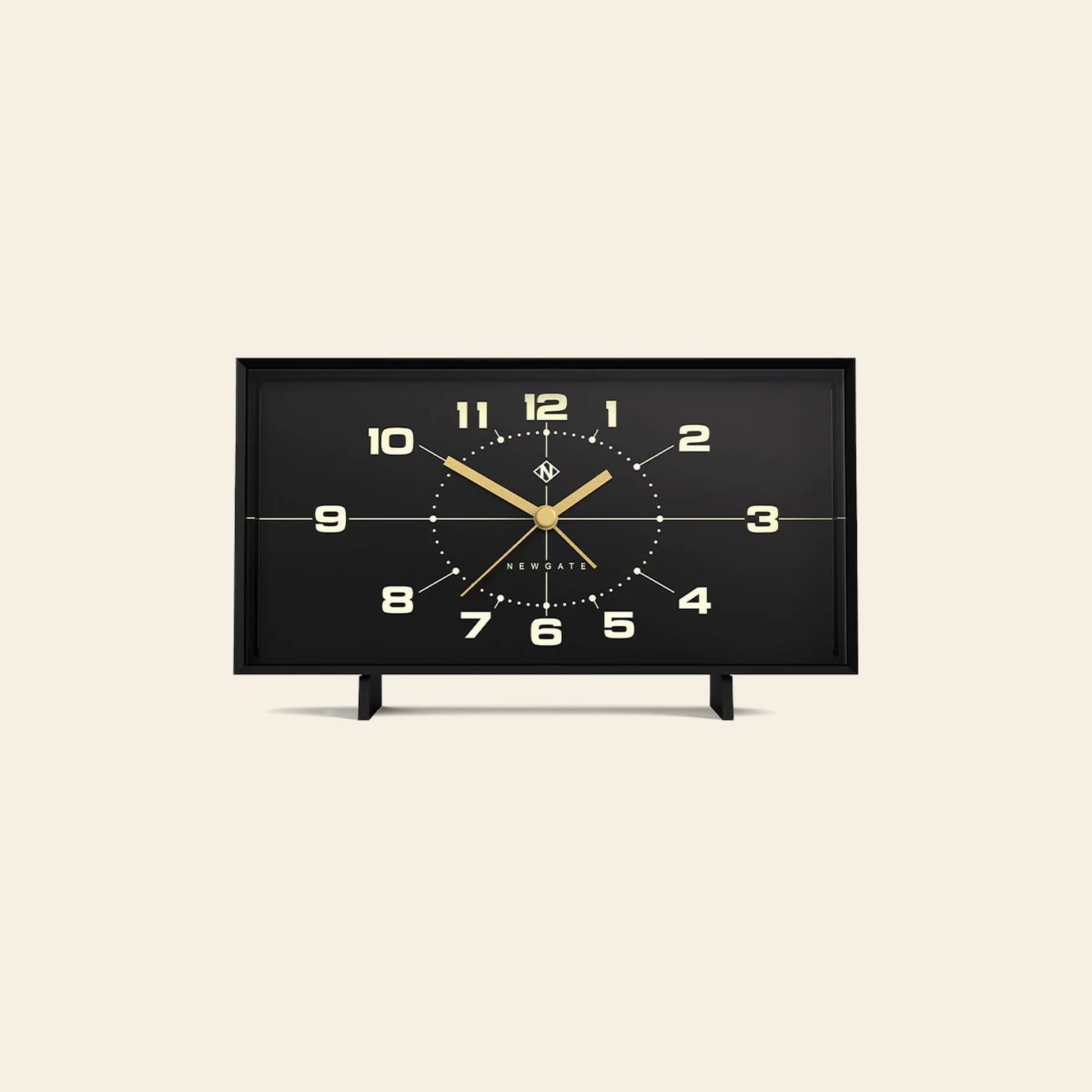 The Newgate Wideboy Alarm Clock by Newgate is a rectangular black clock with gold hands and numbers, a minimalist mid-century atomic dial, and two small legs, shown against a plain beige background.
