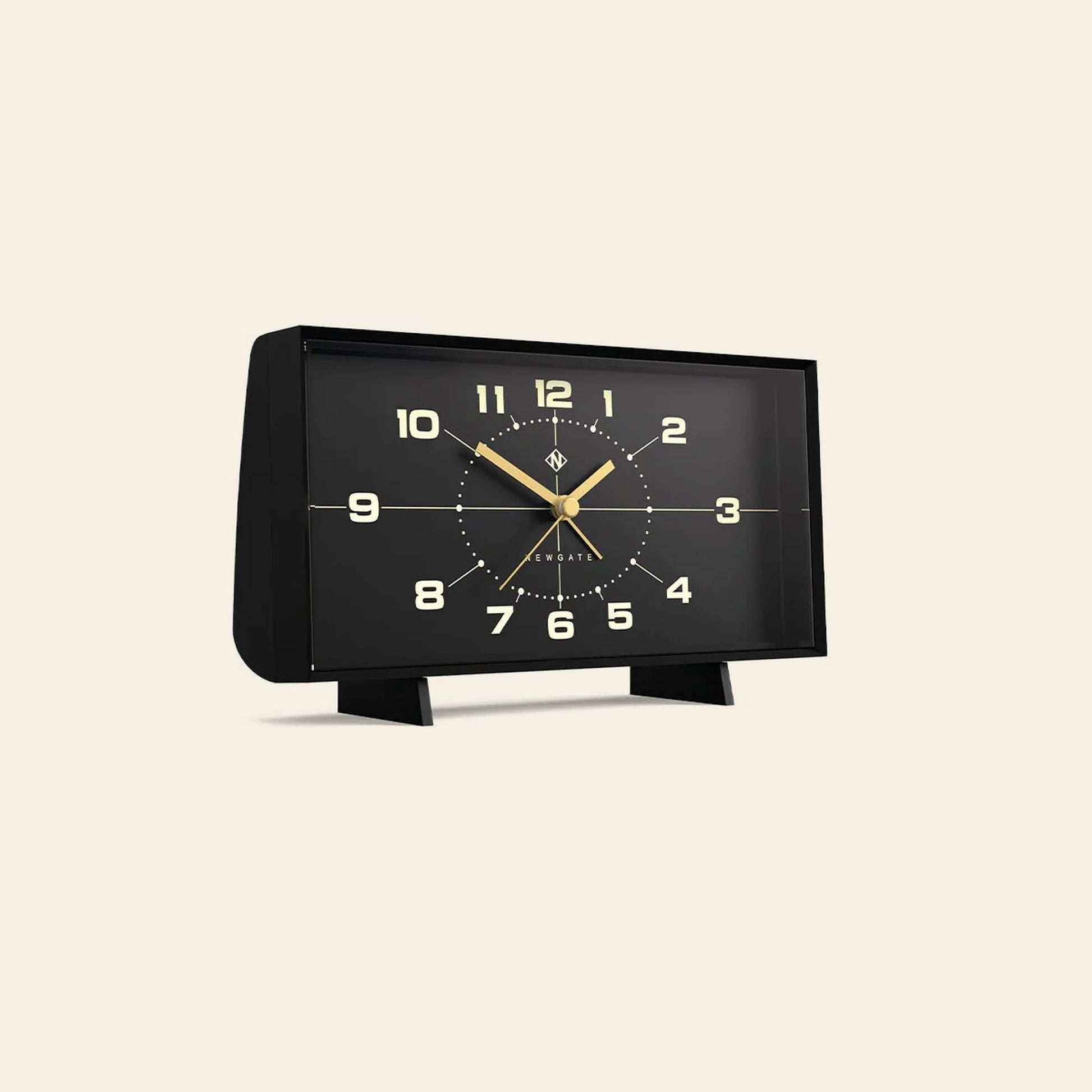 The Newgate Wideboy Alarm Clock by Newgate is a rectangular black clock with gold hands and numbers. Retro-inspired with a modern, minimalist design, it stands on two short legs against a beige background.