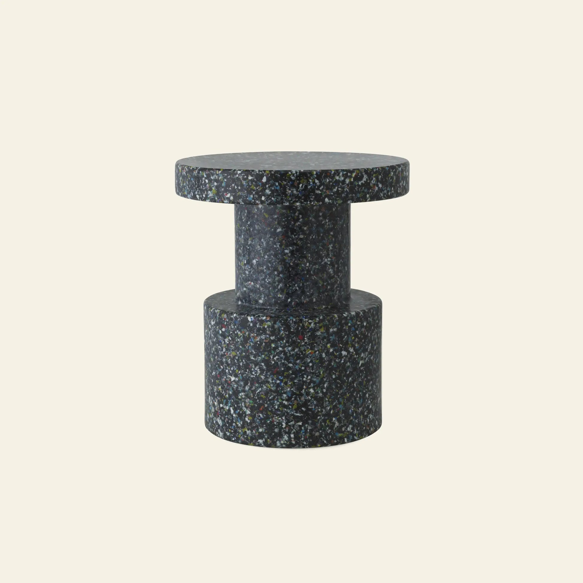 The Normann Copenhagen Bit Stool by Normann Copenhagen features a modern cylindrical shape with a terrazzo-style multicolored speckled finish on a dark base, showcased as versatile seating against a plain light beige background.