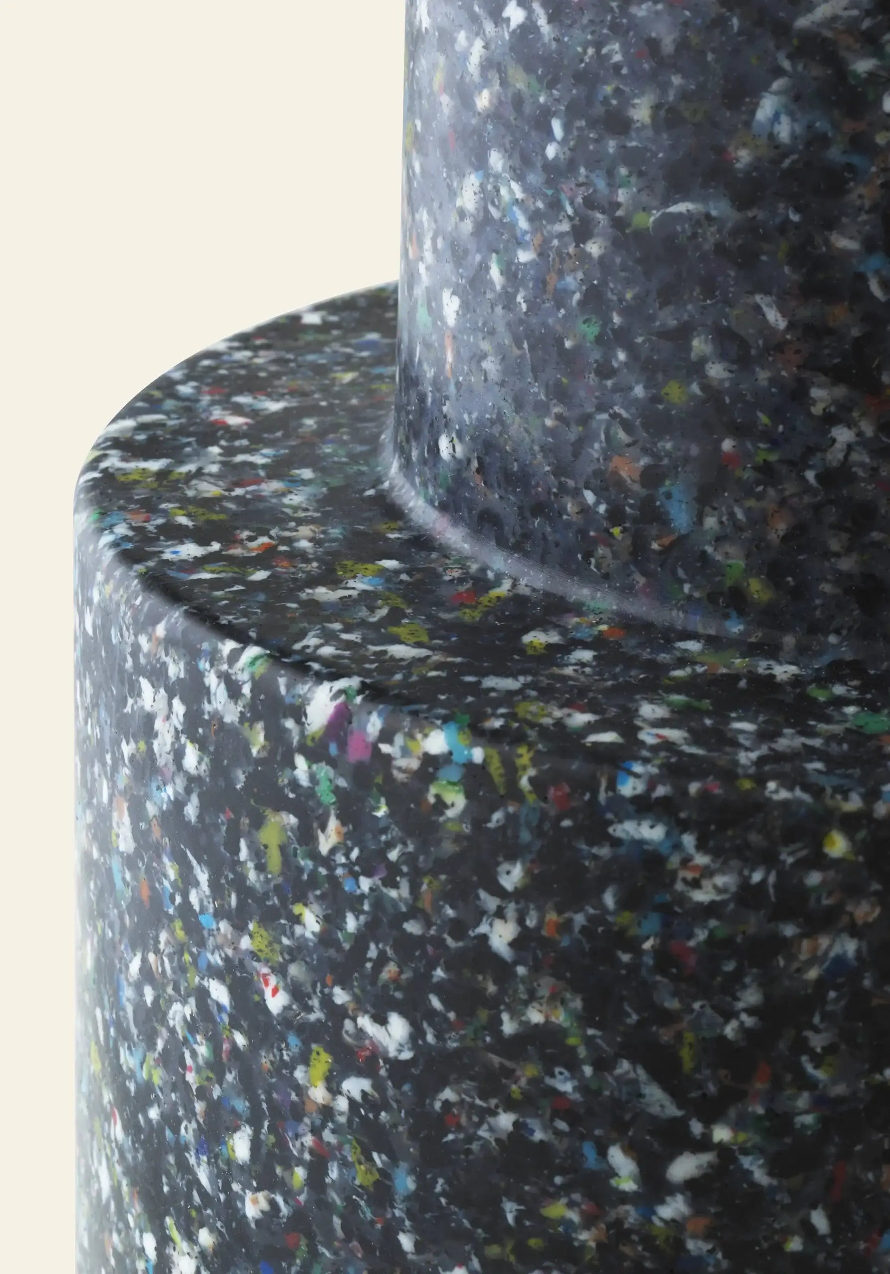 Close-up of the Normann Copenhagen Bit Stool, featuring a terrazzo-inspired surface with small, colorful specks on dark material. This multifunctional piece by Normann Copenhagen has smooth, rounded edges and a matte finish.