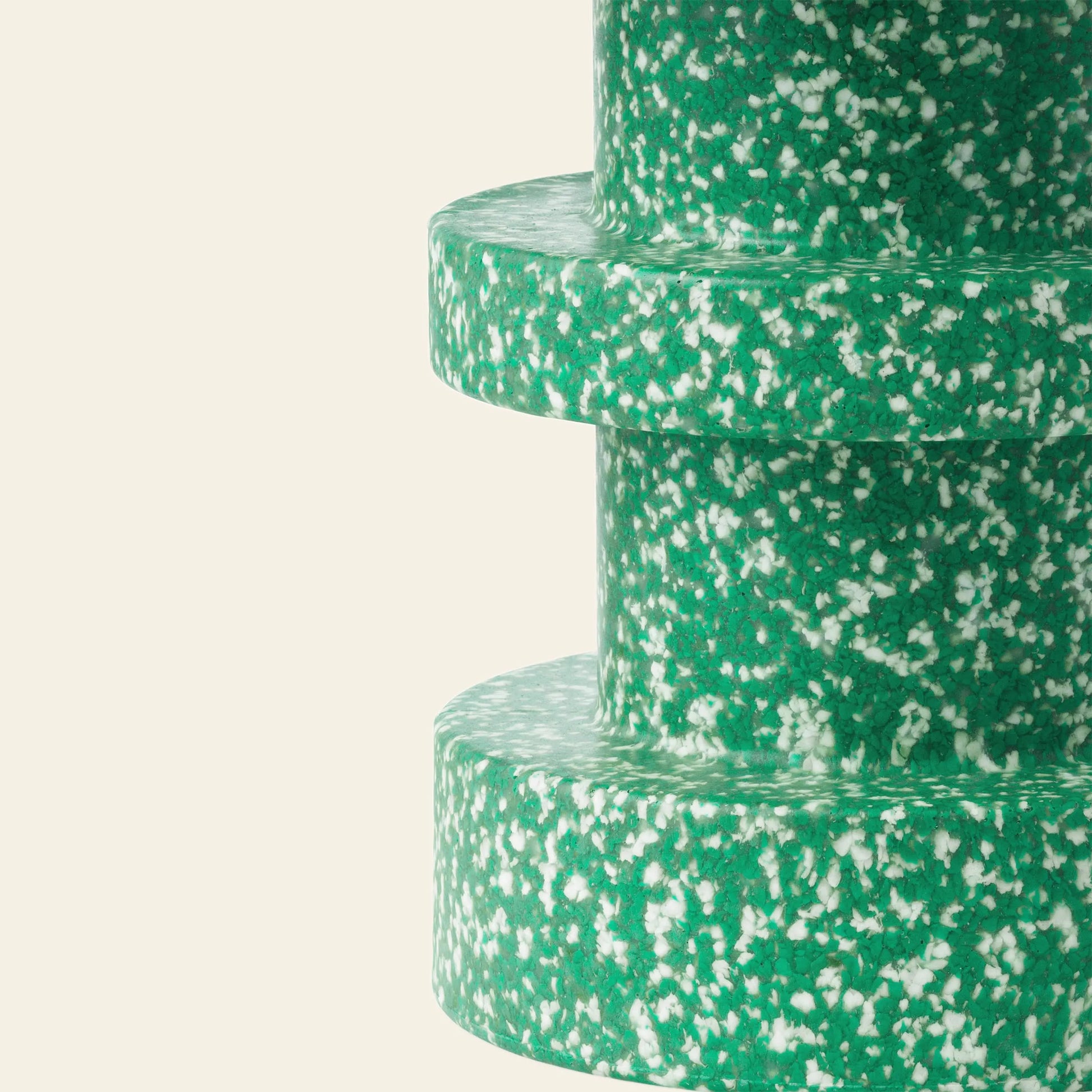 Close-up of Normann Copenhagen Bit Stool Stack, a three-tiered cylindrical stool with a green, white, and yellow speckled finish that resembles terrazzo or recycled plastic, shown against a plain beige background.