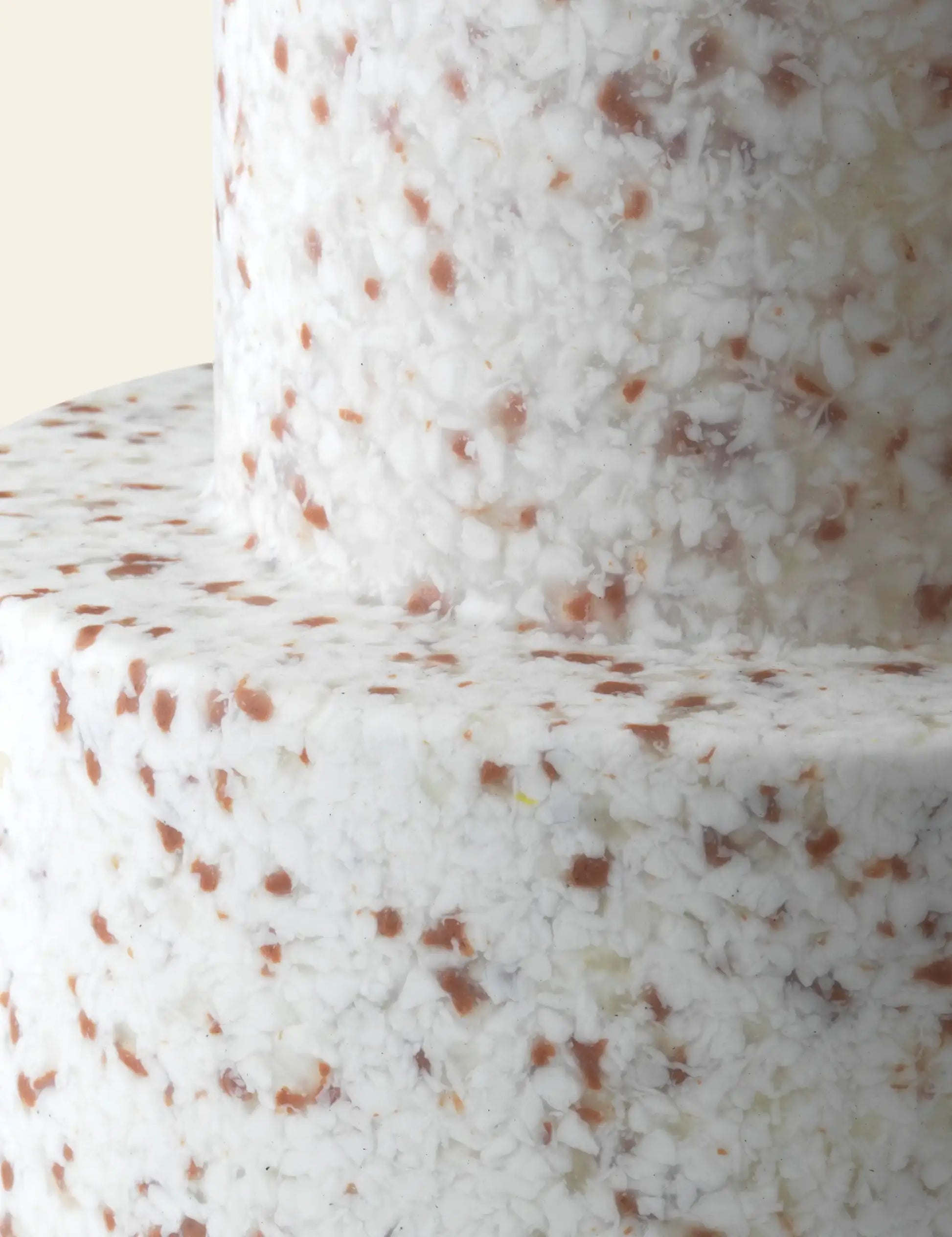 Close-up of a two-tiered cake with a textured white surface dotted with brown and tan bits, echoing the versatile design of the Normann Copenhagen Bit Stool by Normann Copenhagen.