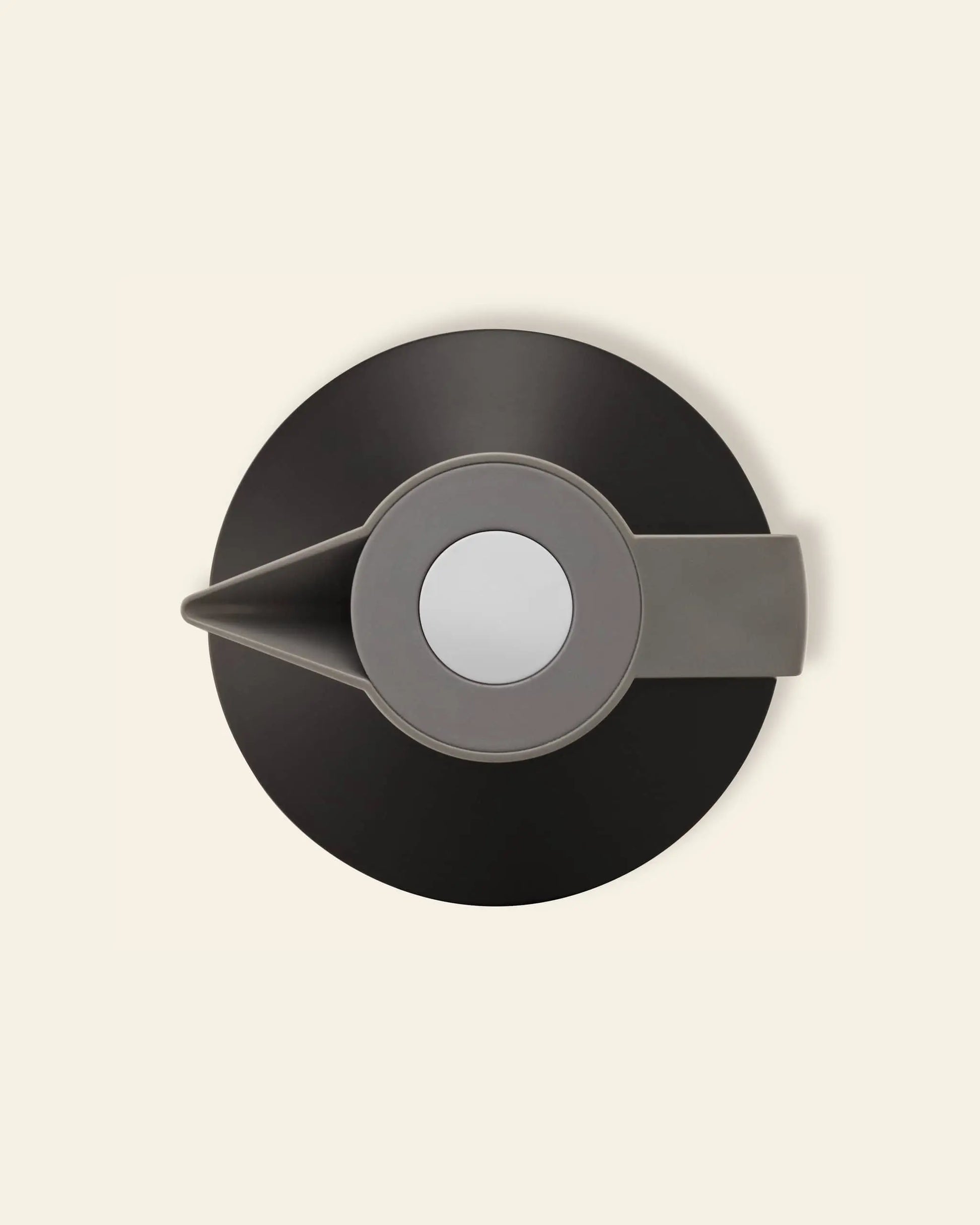 The Normann Copenhagen Geo Vacuum Jug, in grey and black, is seen from above with its round lid, spout, and handle. Its vacuum-insulated body by Normann Copenhagen keeps drinks hot or cold for hours against a beige background.