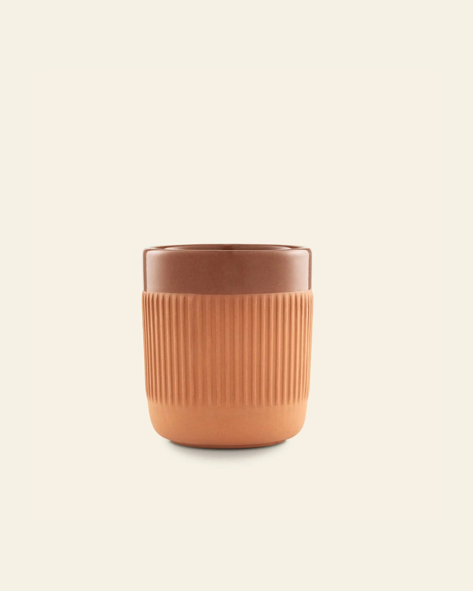 The Normann Copenhagen Junto Cup in warm terracotta features a glossy top and matte, ribbed bottom—ideal for a cozy night in and beautifully set against an off-white background.