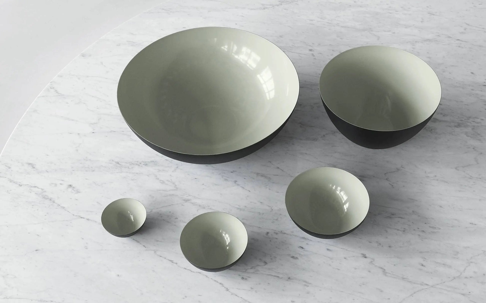 A Normann Copenhagen Krenit Bowl (12.5cm) with a glossy light gray interior and dark exterior rests on white marbleโan elegant touch of Danish design.