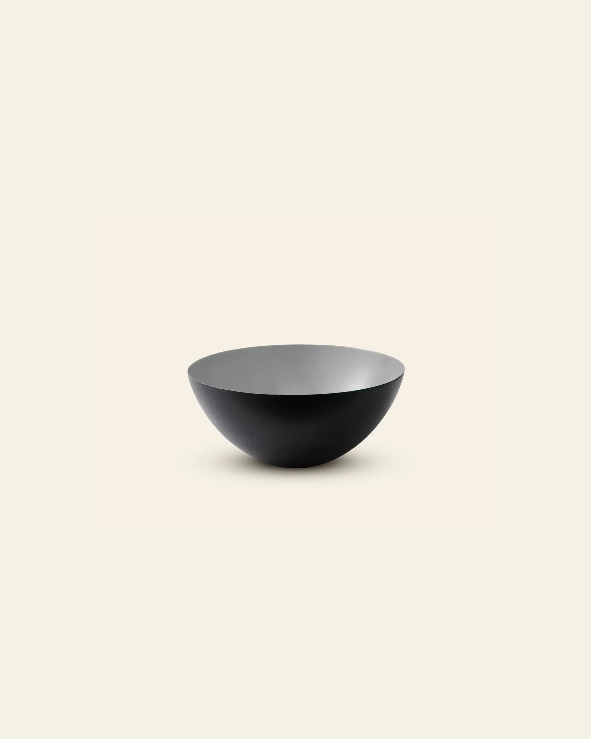 The Normann Copenhagen Krenit Bowl, 12.5cm, features a simple round form and matte black finish, exemplifying timeless Danish design. It is displayed against a plain light beige background.