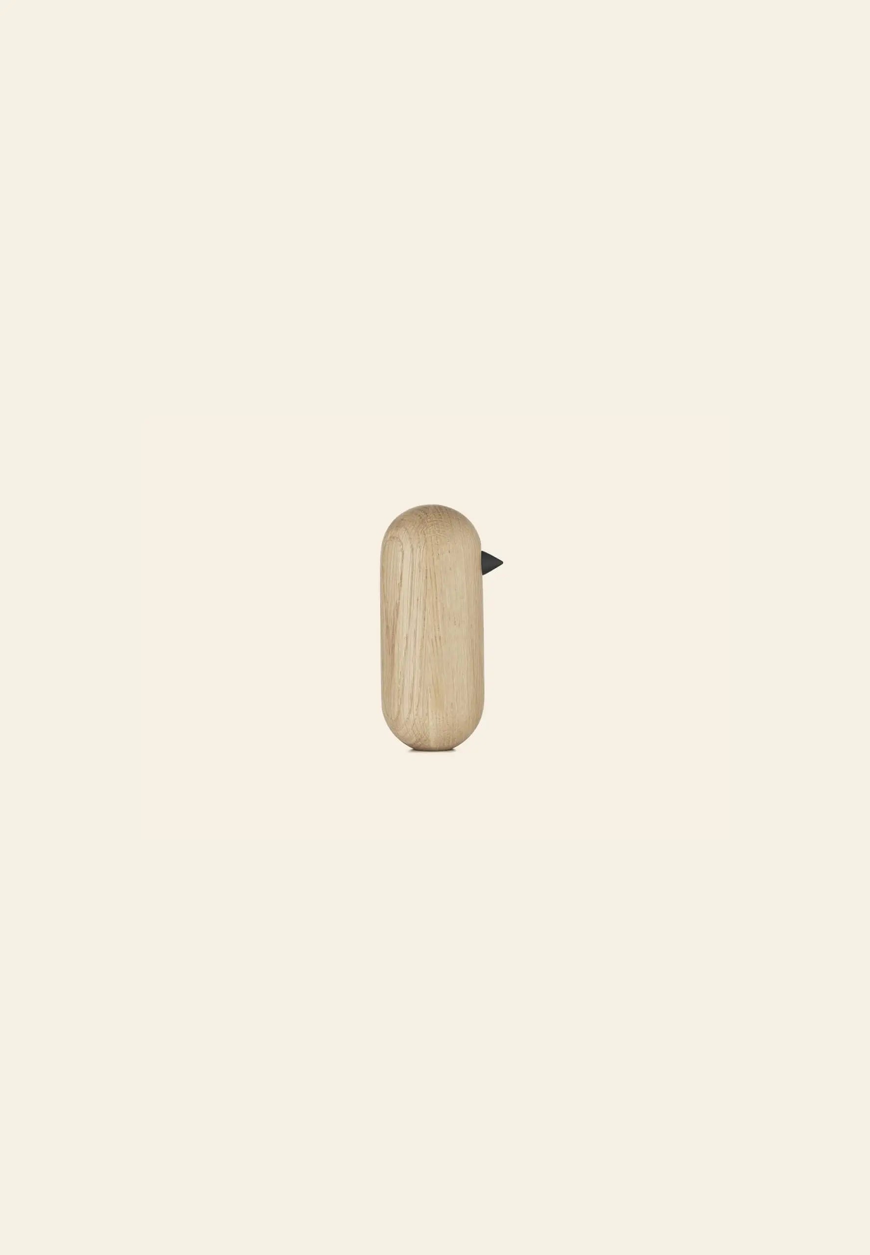 The Normann Copenhagen Little Bird, 13.5cm, features a minimalist wooden design with a smooth rounded body and small black beak, making a stylish decorative accent against a plain light beige background.