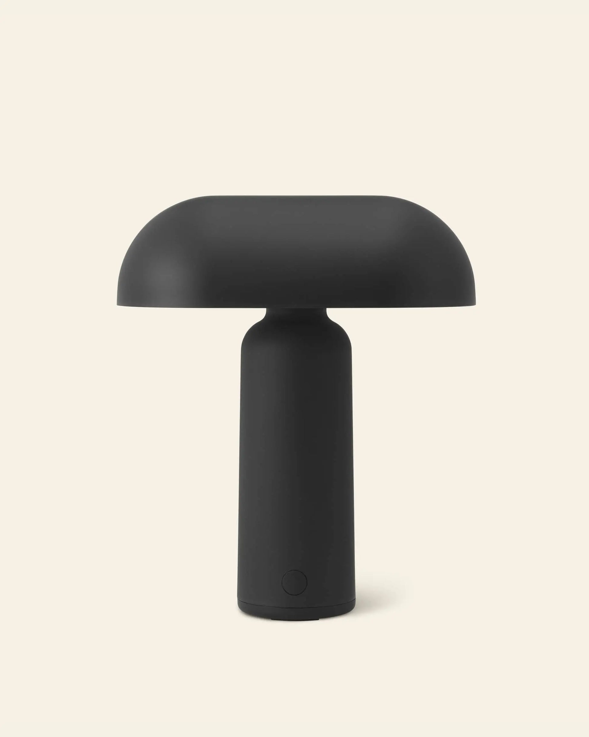 The Normann Copenhagen Porta Table Lamp by Normann Copenhagen features a minimalist black design with a cylindrical base and dome-shaped shade, shown against an off-white background.