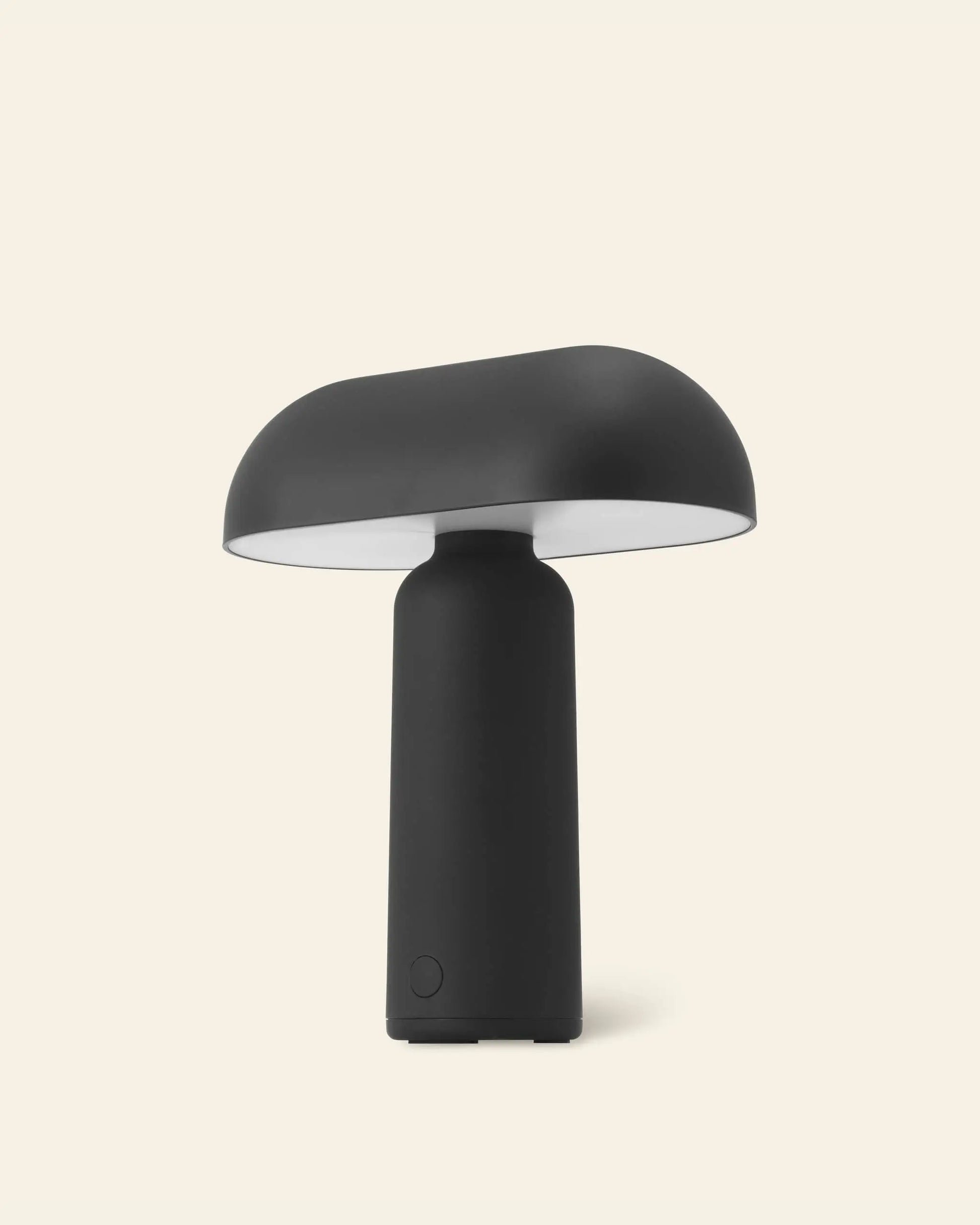The Normann Copenhagen Porta Table Lamp by Normann Copenhagen features a modern matte black finish, mushroom-shaped shade, and cylindrical base, displayed against a plain light beige background.