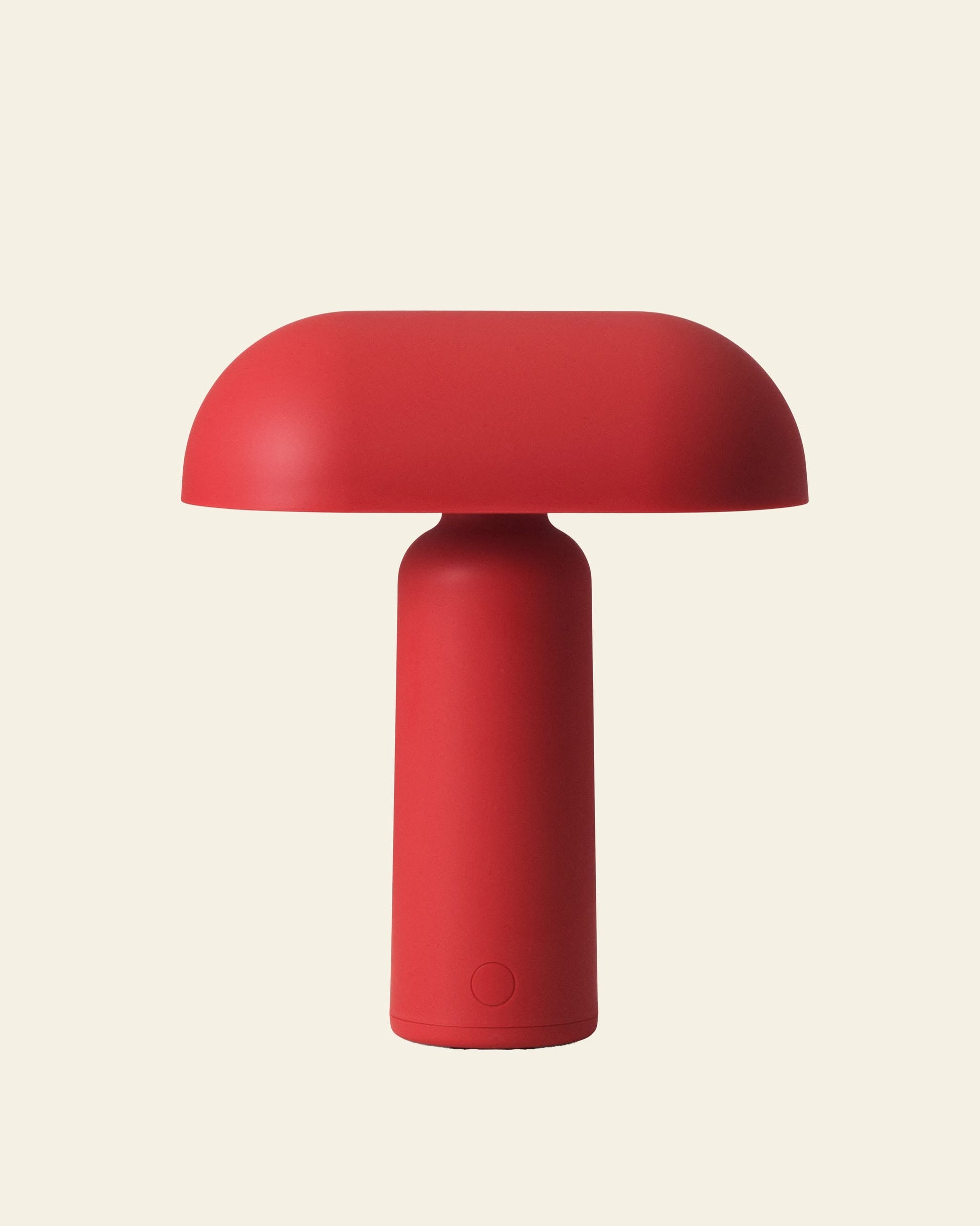 The Normann Copenhagen Porta Table Lamp by Normann Copenhagen is a modern, minimalist red lamp featuring a cylindrical base and rounded dome top, shown against a plain light beige background.
