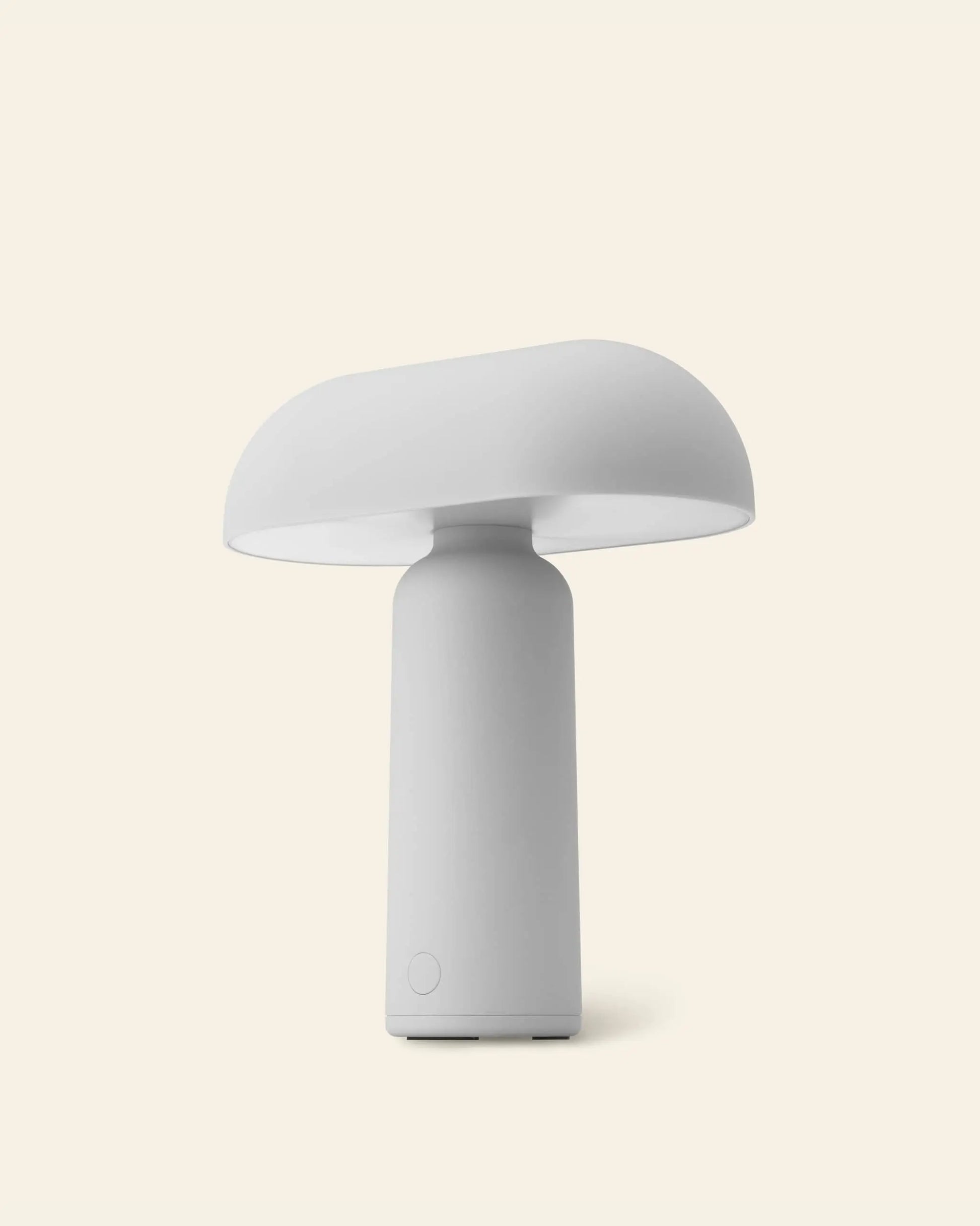 The Normann Copenhagen Porta Table Lamp features a minimalist white design with a rounded, mushroom-style shade and cylindrical base, exemplifying modern style against a light beige background.