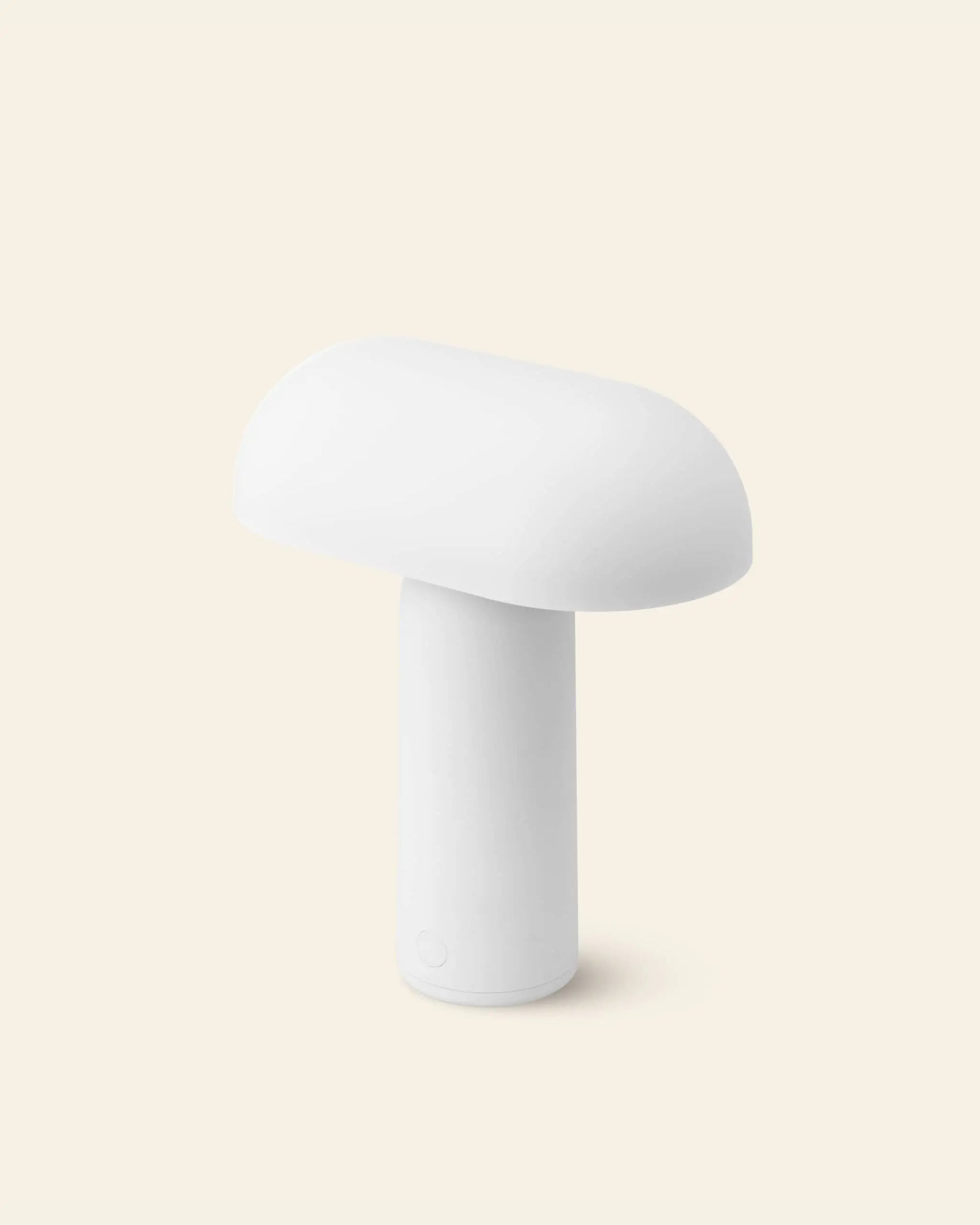 The Normann Copenhagen Porta Table Lamp by Normann Copenhagen, featuring a minimalist white mushroom shape with a rounded top and cylindrical base, stands upright against a plain light beige background.