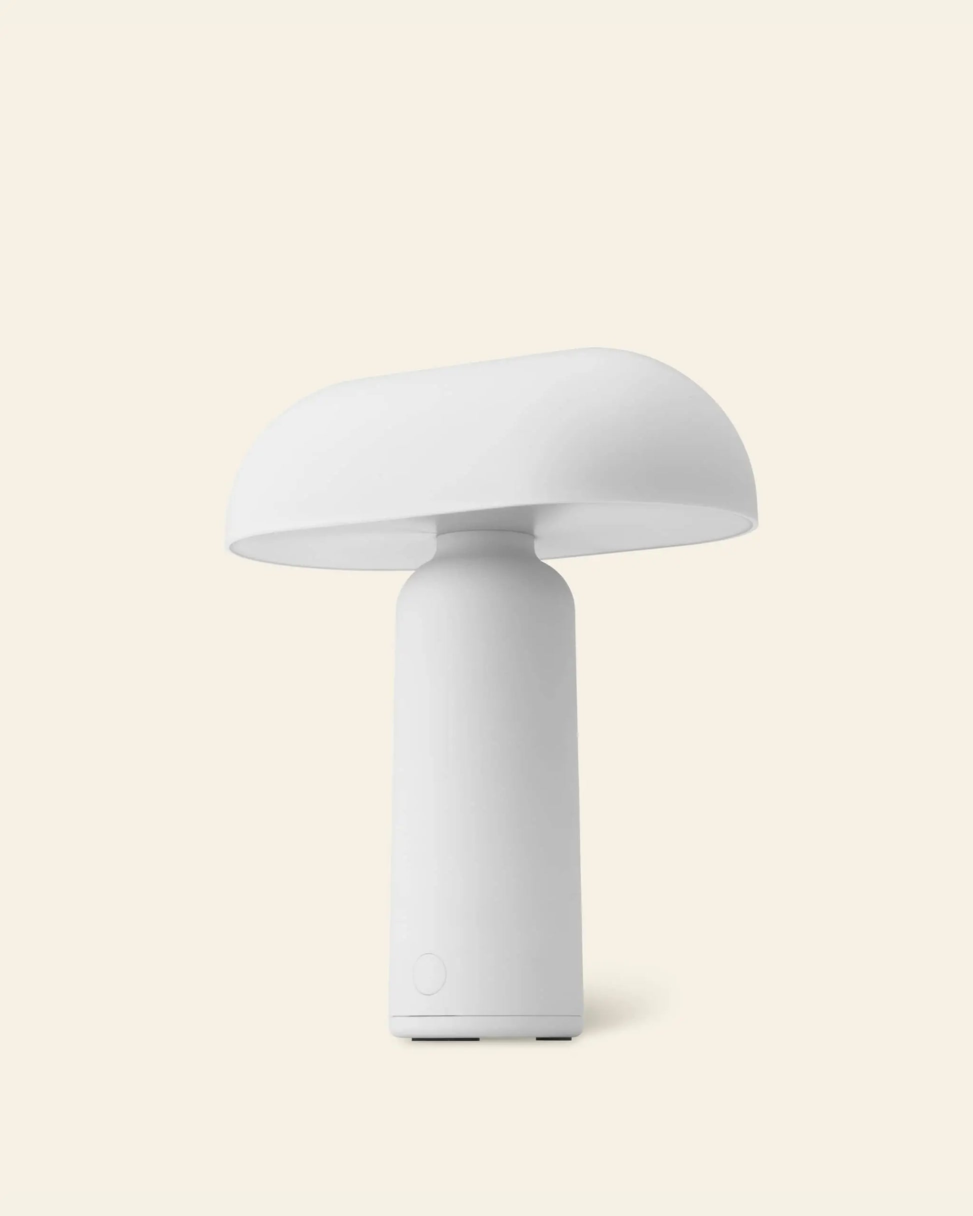 The Normann Copenhagen Porta Table Lamp features a modern, minimalist white design with a cylindrical base and wide rounded top, capturing Normann Copenhagen’s signature style against a light beige background.