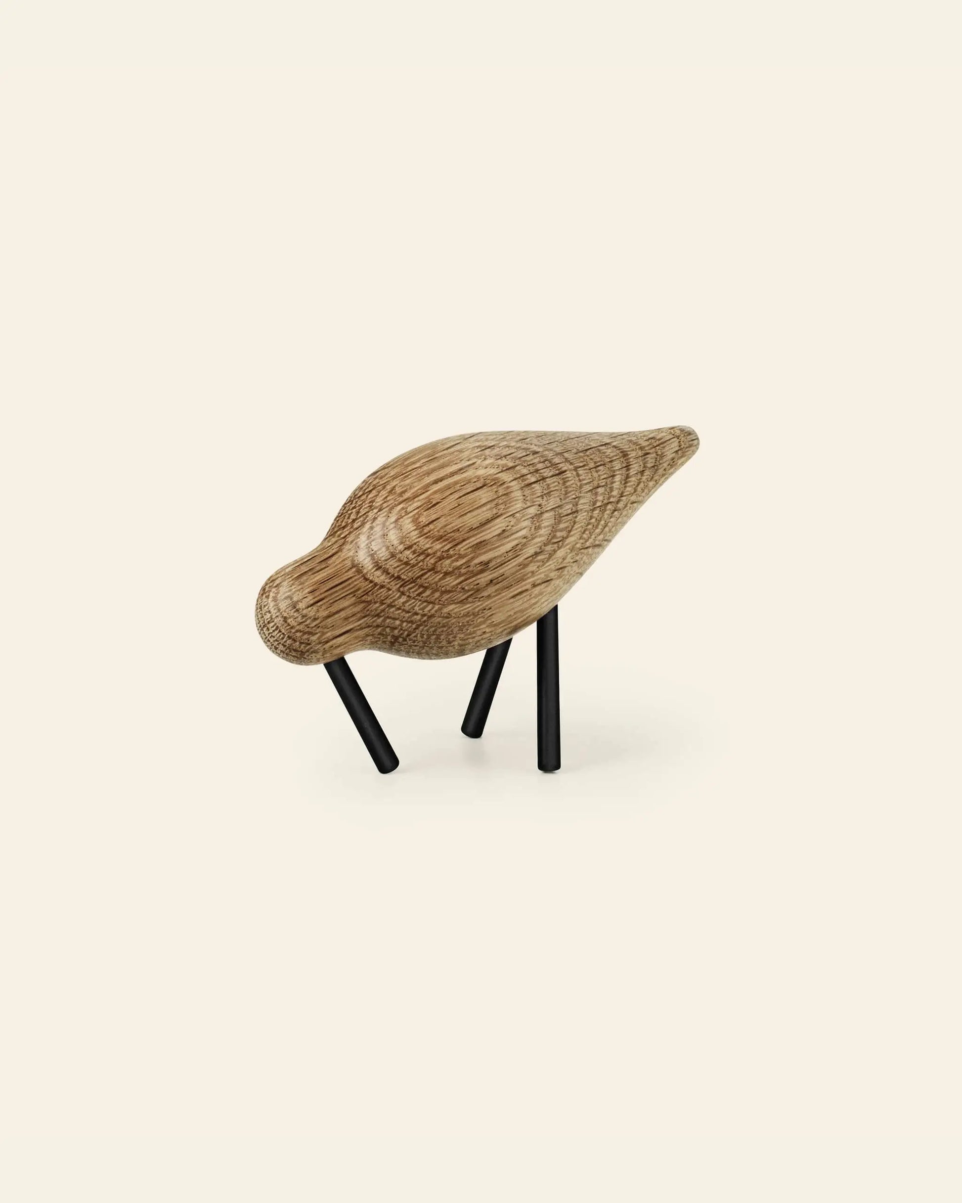 The Normann Copenhagen Shorebird Small Oak sculpture by Normann Copenhagen features a smooth, rounded oak body and black metal legs, showcased against a plain, light background.