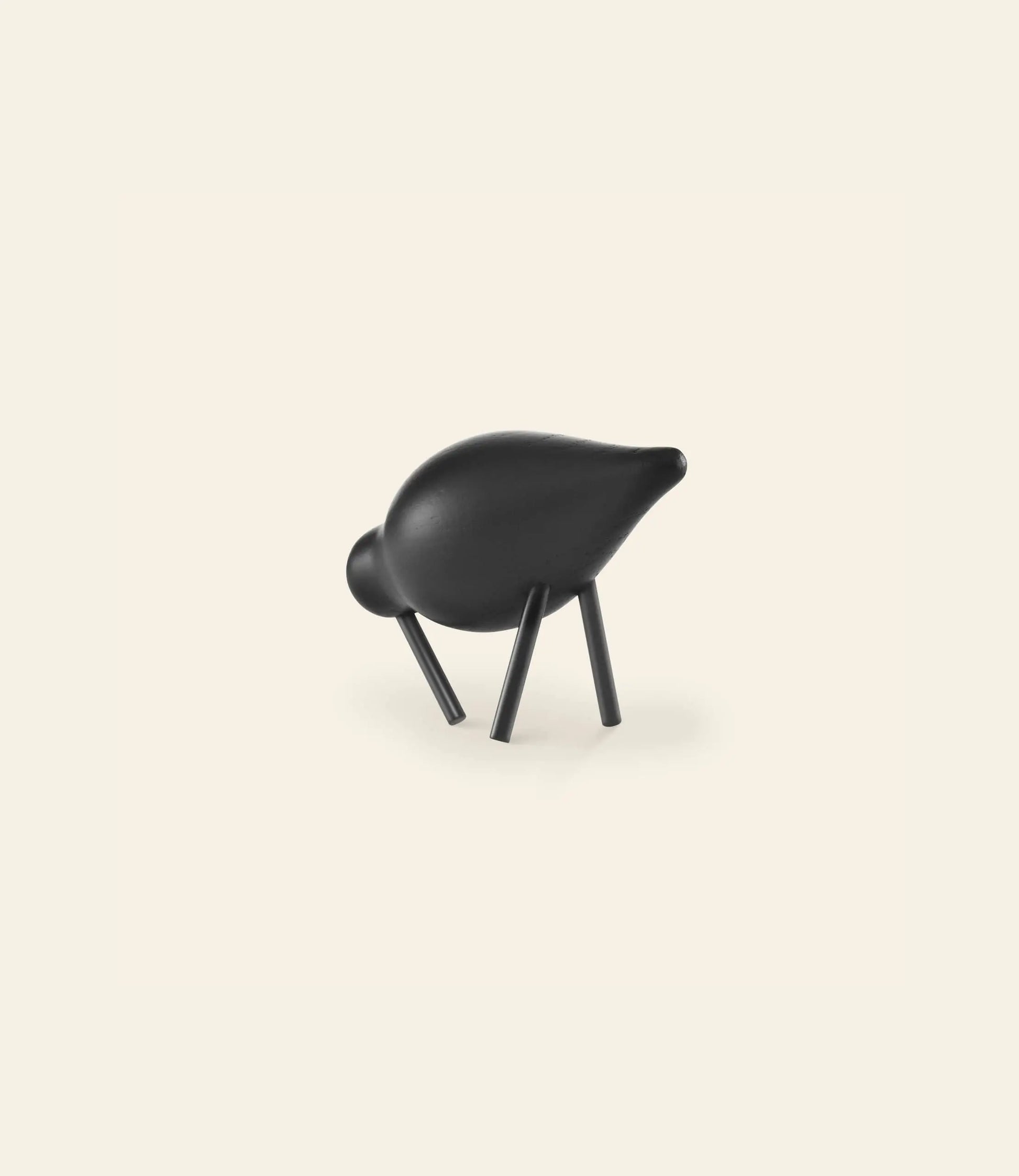 A minimalist black sculpture, reminiscent of the Normann Copenhagen Shorebird Small Oak by Normann Copenhagen, features a stylized animal form with a rounded body and four angled legs, set against an off-white background.