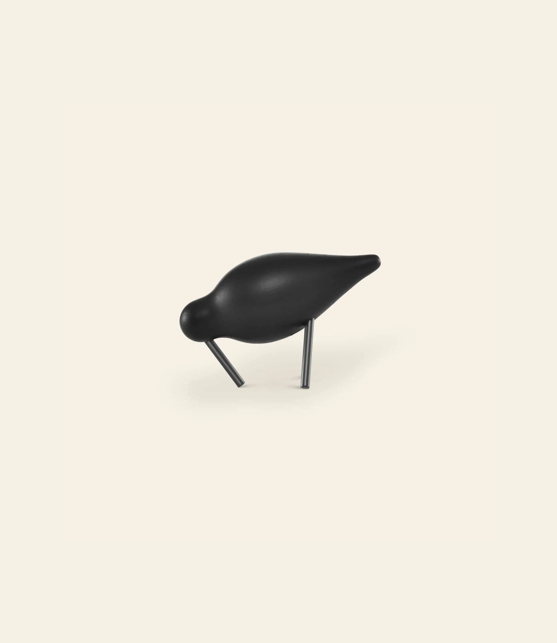 The Normann Copenhagen Shorebird Small Oak is a minimalist black oak wood sculpture with a rounded body and short legs, styled as if pecking the ground, set against a plain, light-colored background.