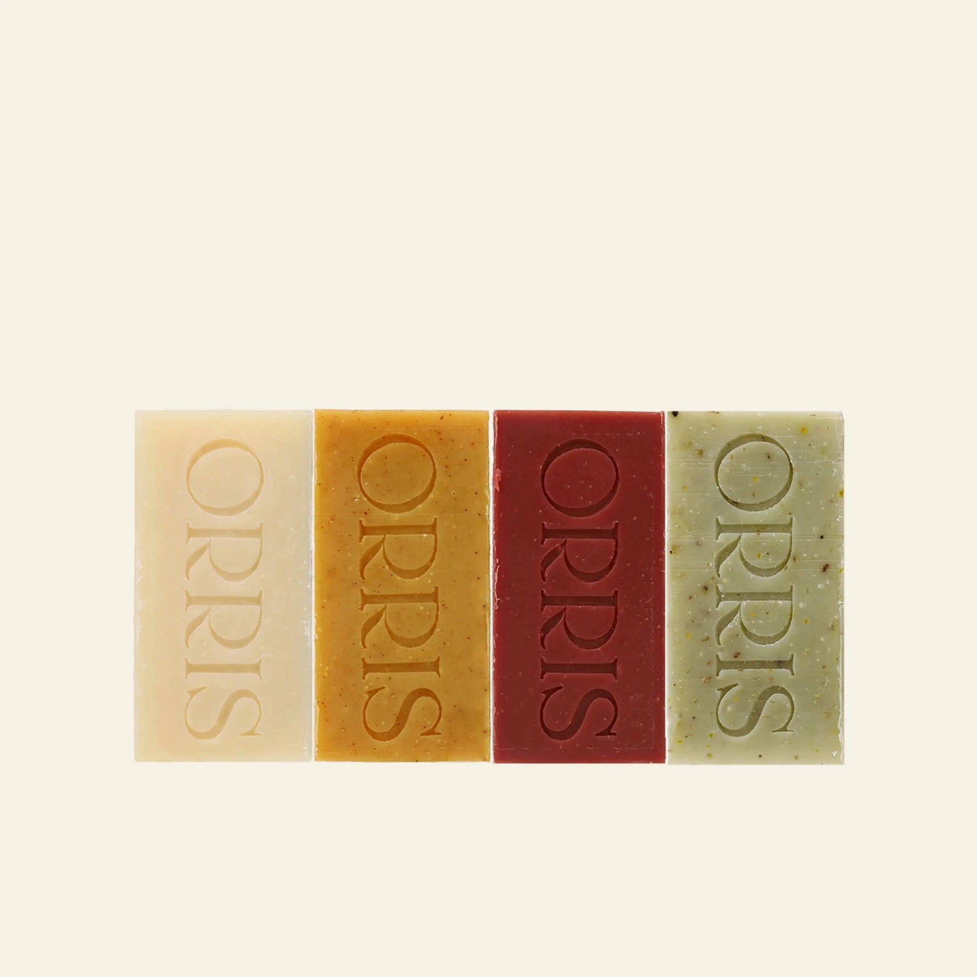 ORRIS Le Quartet by ORRIS features four rectangular cleansing bars—cream, orange, red, and green—each embossed with the brand name. Arranged side by side on a light background, these botanical soaps are crafted for skincare benefits.