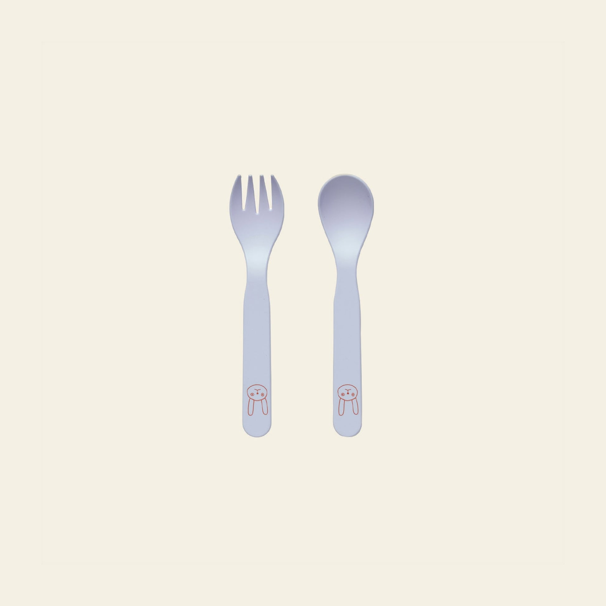A white fork and spoon with rounded edges from the OYOY Living Design Pullo Cutlery Set are side by side. Each handle features a pink bunny face illustration. The eco-friendly PLA set rests on a pale cream background.