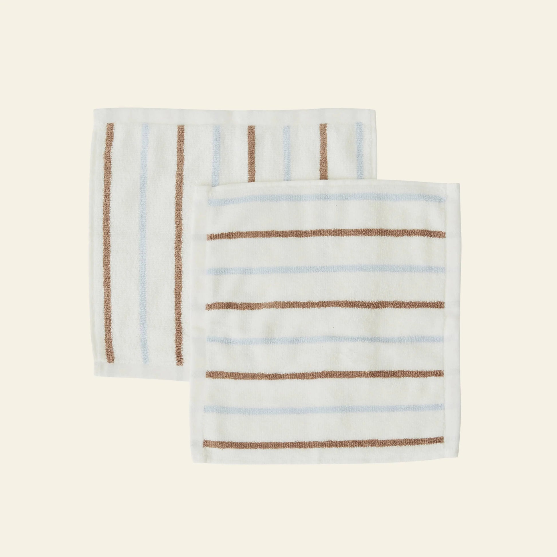 The OYOY Living Design Raita Wash Cloth, Pack of 2, includes organic cotton terry cloths with white borders: one with thin vertical brown stripes, the other with horizontal brown and subtle blue stripes on a light cream background.