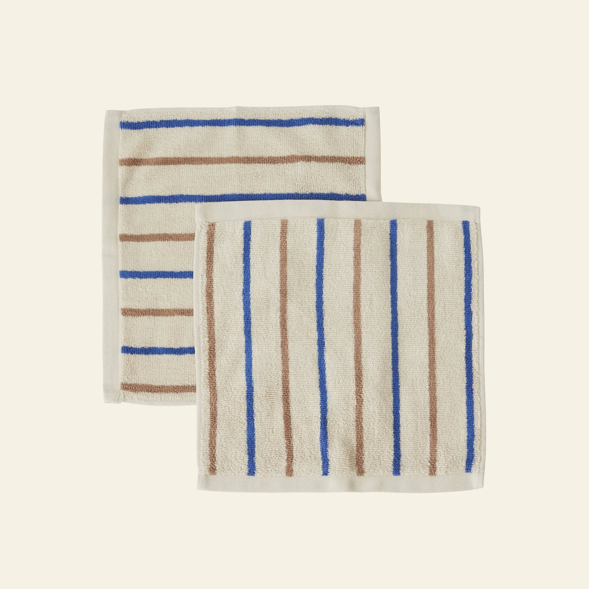 The OYOY Living Design Raita Wash Cloth, Pack of 2, features two organic cotton terry wash cloths with brown and blue stripes—one horizontal, one vertical—on a cream background.