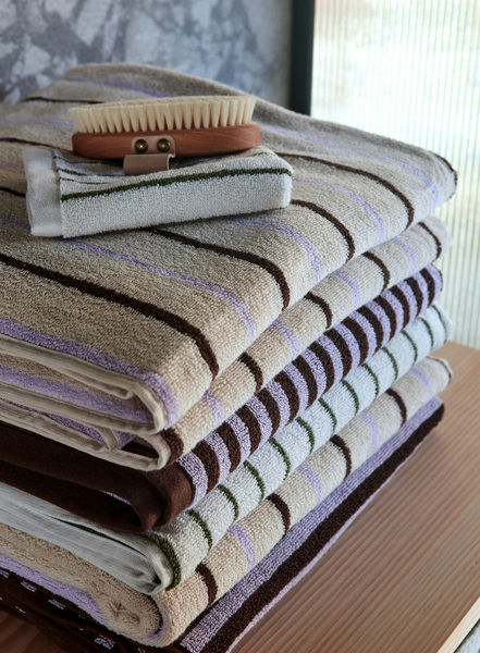 A stack of OYOY Living Design Raita Wash Cloths, Pack of 2, in beige, brown, and white stripes sits on a wooden surface with a wooden bath brush placed on top.