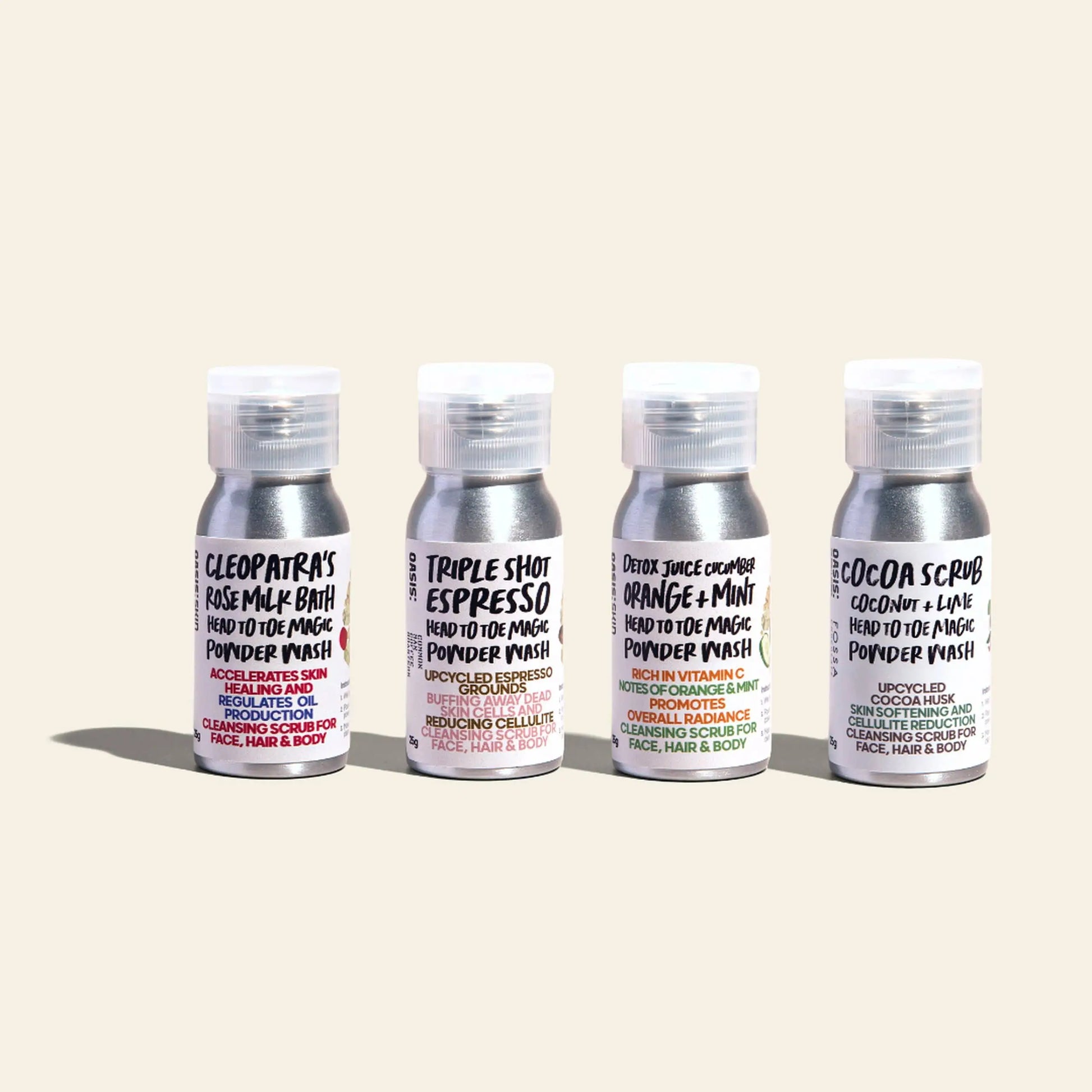 Four bottles of Oasis Beauty Kitchen Head to Toe Magic Powder Wash (25g) are lined up against a light background, each with plant-based ingredients and distinct labels—rose, espresso, orange + mint, and cocoa + lime—for unique formulas.