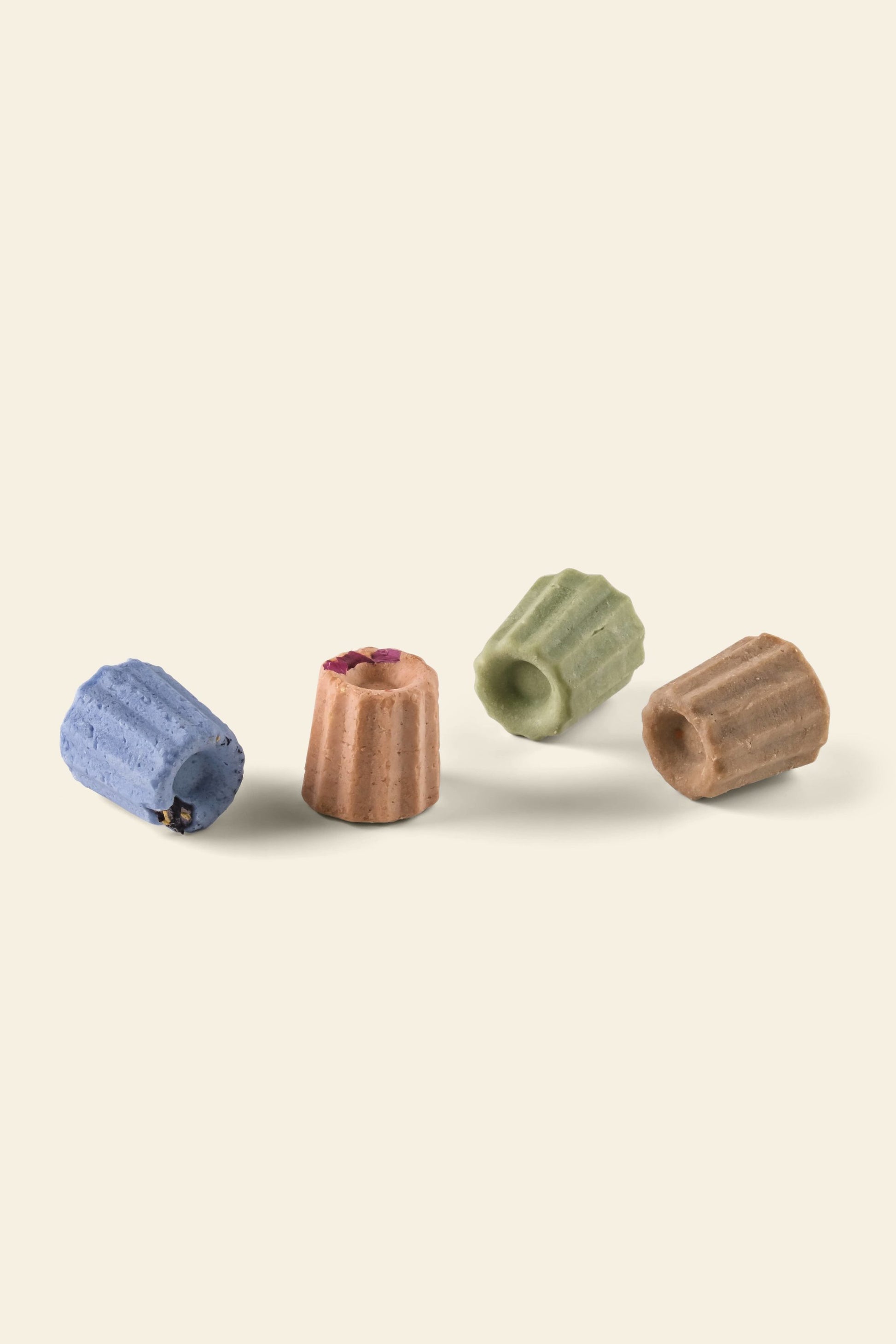 The Oasis Beauty Kitchen Miniature Solid Shampoos Set features four vegan, ridged, cylindrical bars in blue, pink, green, and brown—each with organic herbs for different hair needs—arranged on a light beige background.