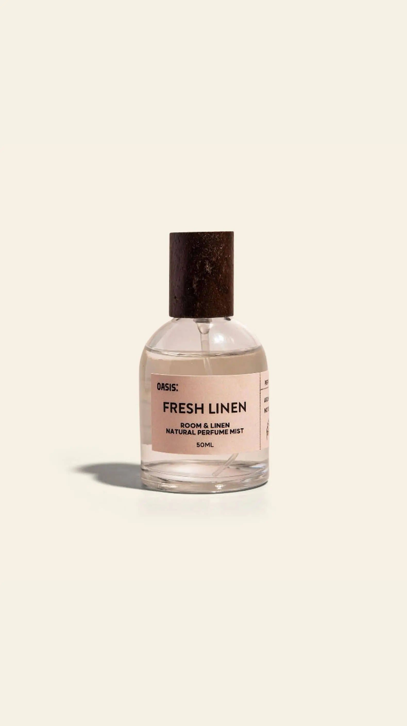 A clear glass bottle with a dark wooden cap labeled Oasis Beauty Kitchen Room and Linen Mist, 50ml sits against a light background, highlighting the fresh linen scent of this premium mist from Oasis Beauty Kitchen for home and linens.