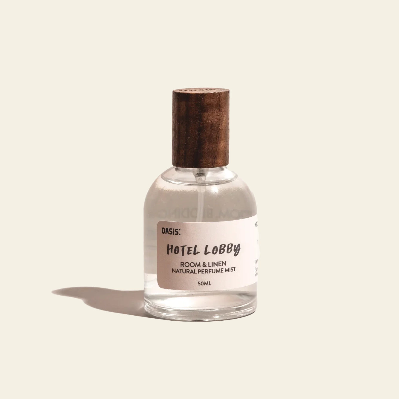 A small clear bottle with a wooden cap labeled Oasis Beauty Kitchen Room and Linen Mist, 50ml stands on a beige background, casting a shadow to the left. Enjoy this refreshing, perfume-grade mist with a subtle fresh linen scent from Oasis Beauty Kitchen.