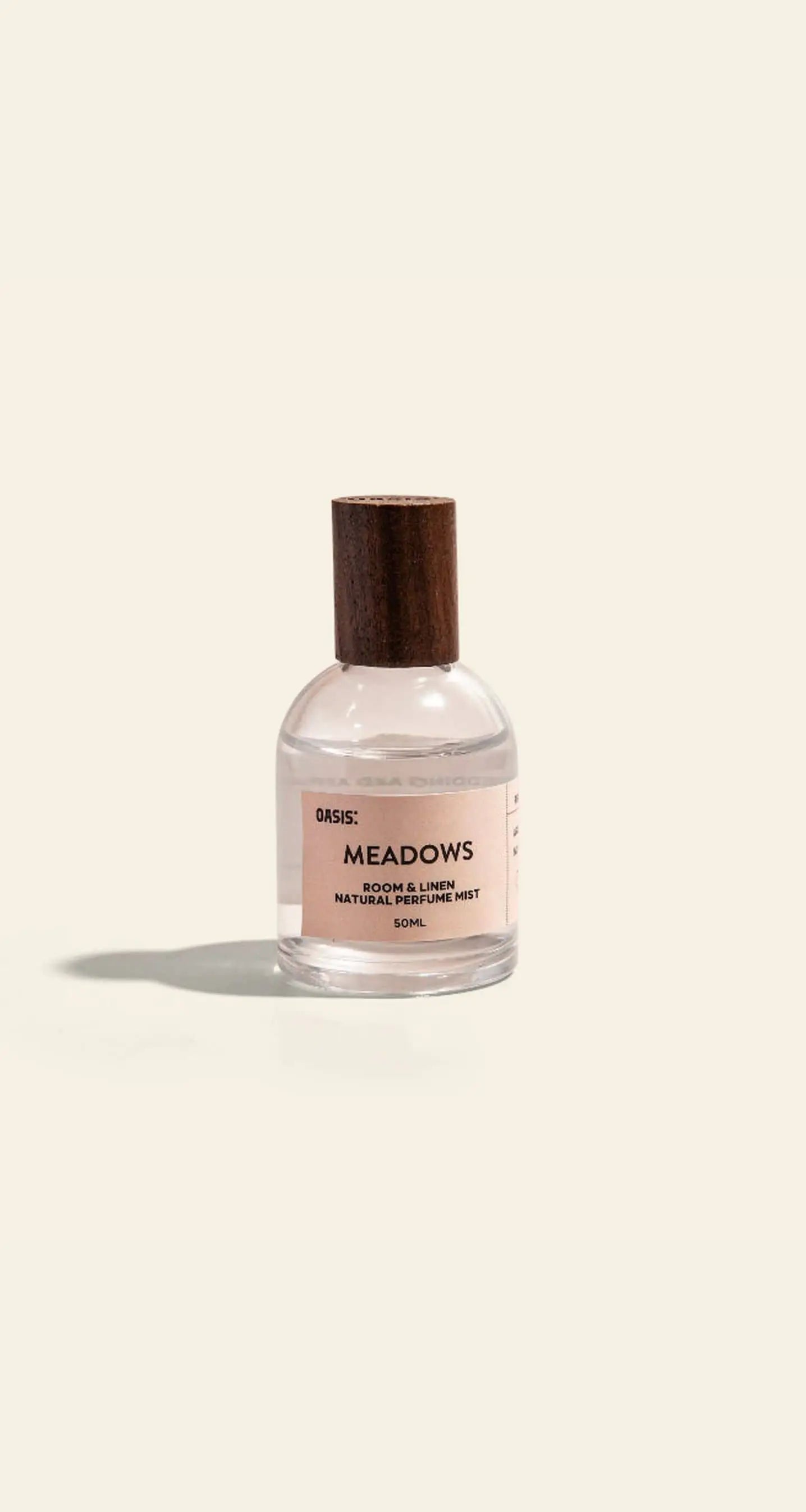 A clear 50ml Oasis Beauty Kitchen Room and Linen Mist bottle with a wooden cap sits against a plain light background, releasing a fresh linen scent in this perfume-grade mist by Oasis Beauty Kitchen.