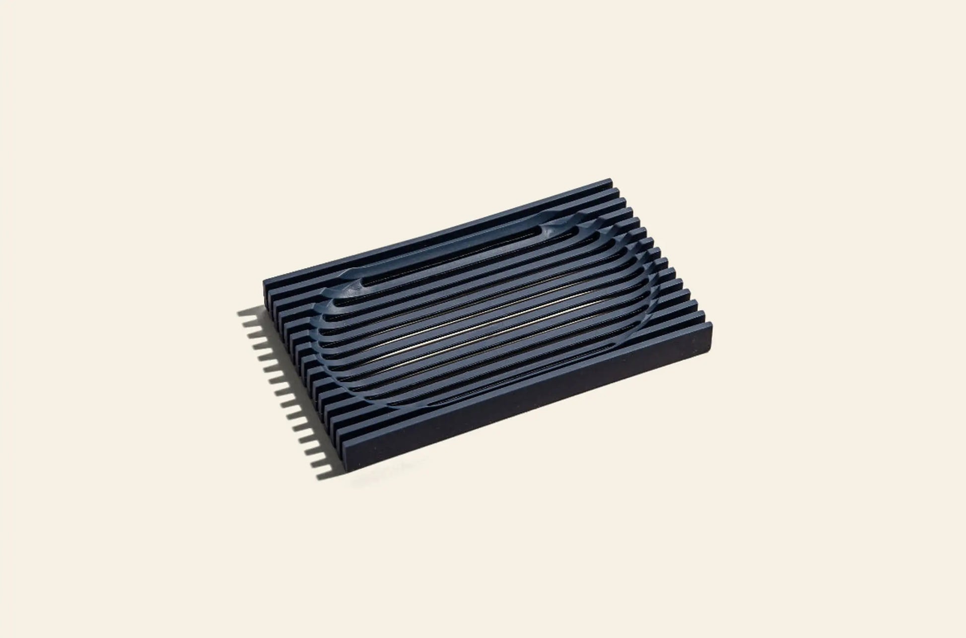 The Oasis Beauty Kitchen The Lattice Soap Dish by Oasis Beauty Kitchen features a black rectangular design with raised curved and straight ridges, crafted for durability and ideal for everyday zero waste living. Photographed on a plain beige background.