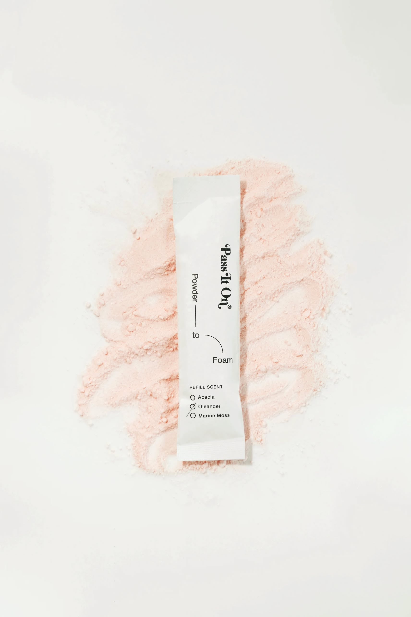 A Pass It On 0.02 Refillable Hand Wash Set, Single Pack - Oleander by Pass It On rests on a mound of light pink botanical powder. The packet highlights refill scents for sustainable hand hygiene: Acacia, Osmanthus, Gardenia, Marine Musk.