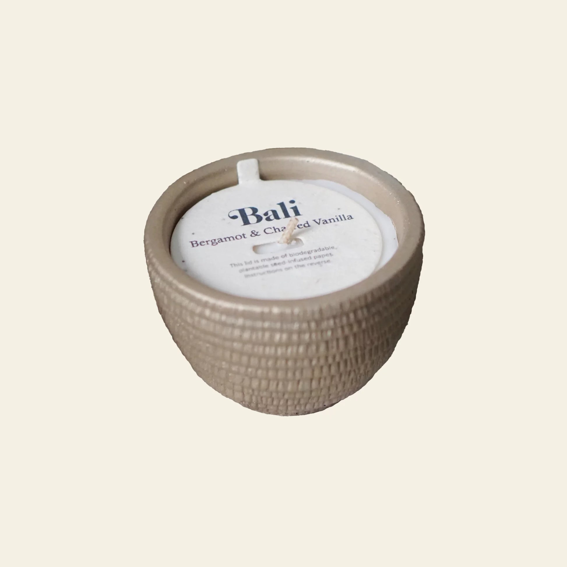 The Pass It On Bali Candle by Pass It On is a beige, textured candle in a round ceramic jar labeled Bali, featuring bergamot and charred vanilla fragrance. Unused with a single wick centered.