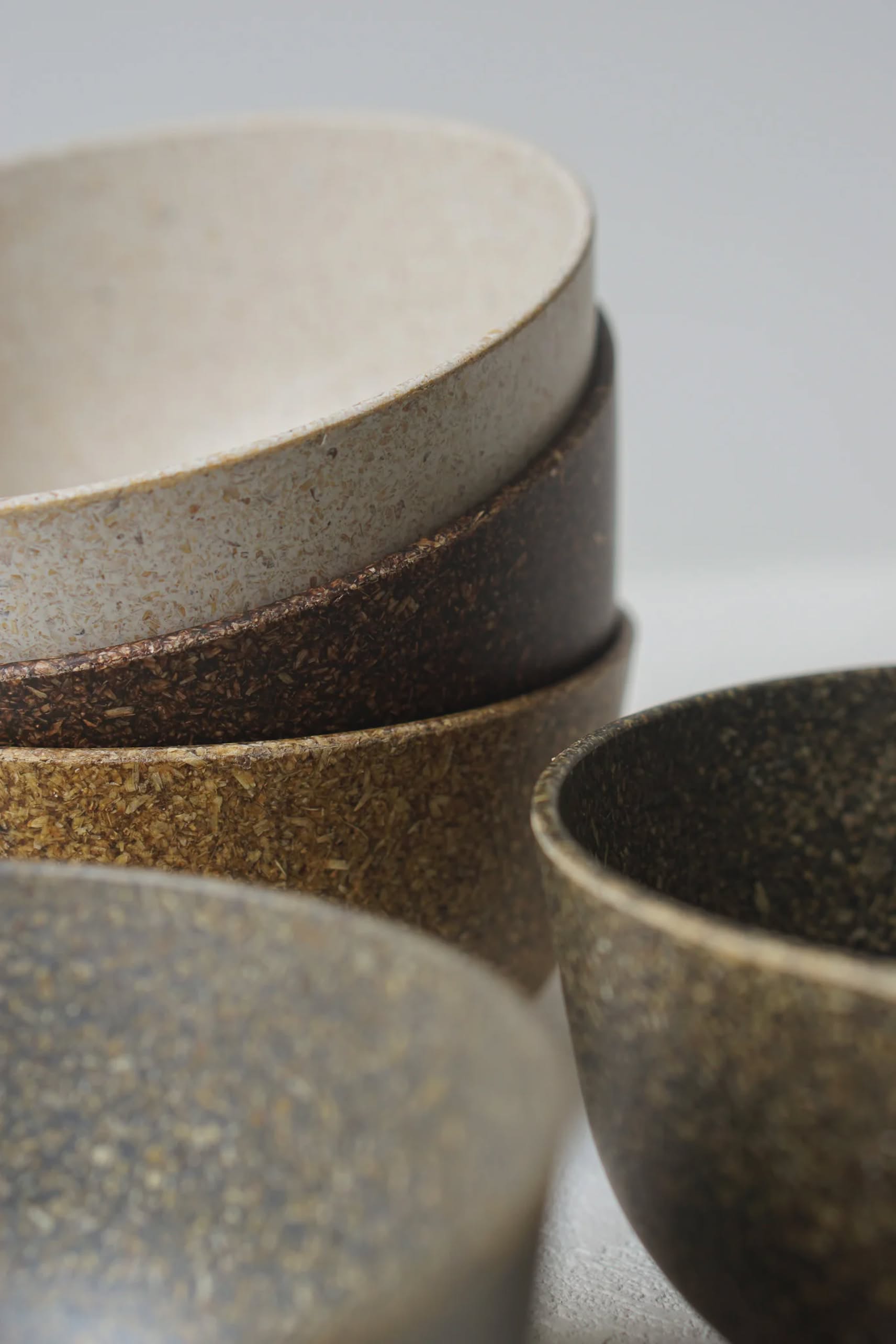 A close-up of stacked and nested Pass It On Capsule Bowls, Rice Husk, in earthy brown, cream, and dark speckled tones, highlights their textured surfaces—crafted by Pass It On from upcycled rice husks—for a sustainable touch.