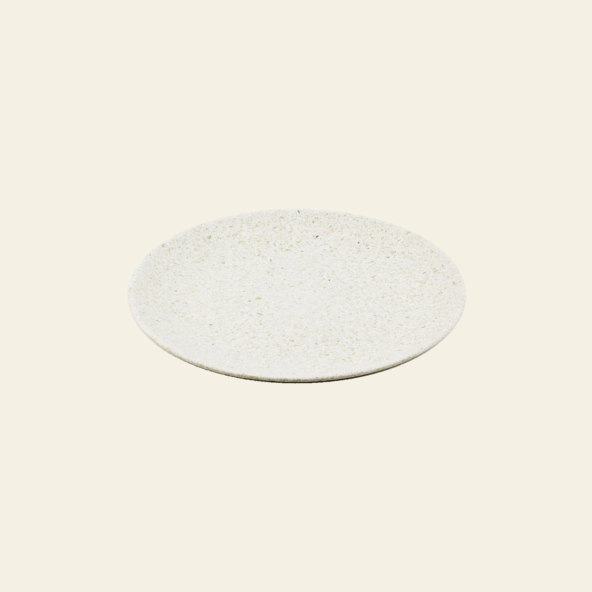 The Pass It On Dining Plate M, Rice Husk by Pass It On is a round, off-white ceramic plate with a subtly textured surface and modern design, providing an eco-friendly choice for sustainable dining. Shown on a plain light beige background.