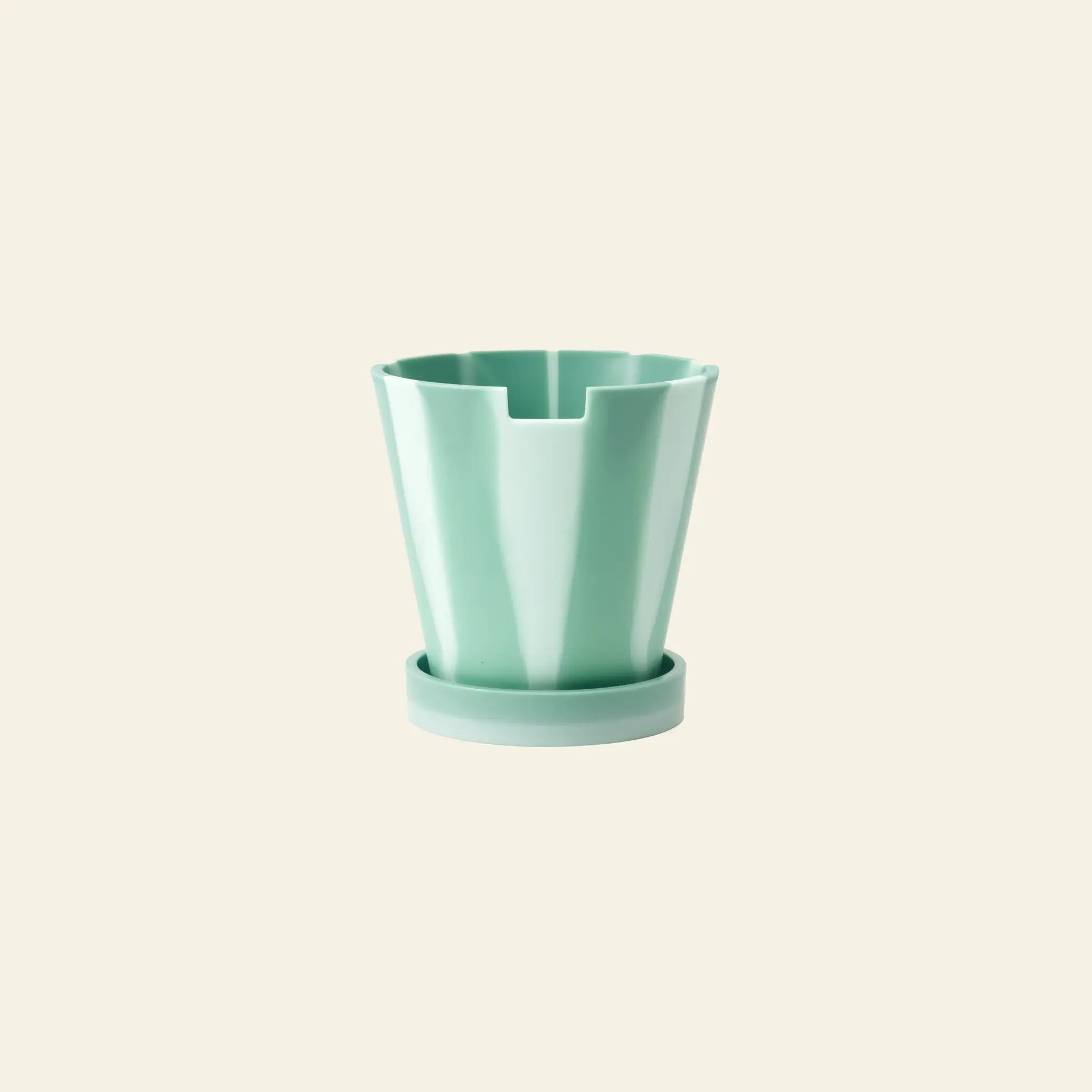 The Plastic Ark Dirty Pot by Plastic Ark is a mint green, angular recycled plastic pot with vertical grooves on a matching saucer, shown against a plain beige background.
