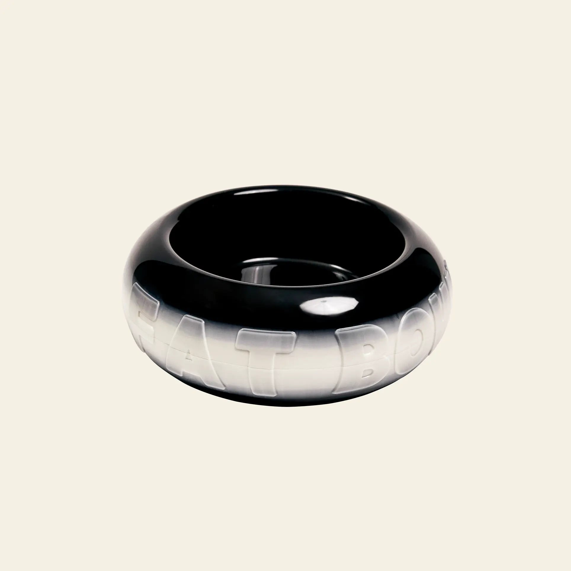 A glossy, black, round Plastic Ark Fat Bowl by Plastic Ark with raised white FAT BOWL text wraps the exterior. Its customizable design lets you add a personal touch to your pet’s dining space. Set against a plain off-white background.