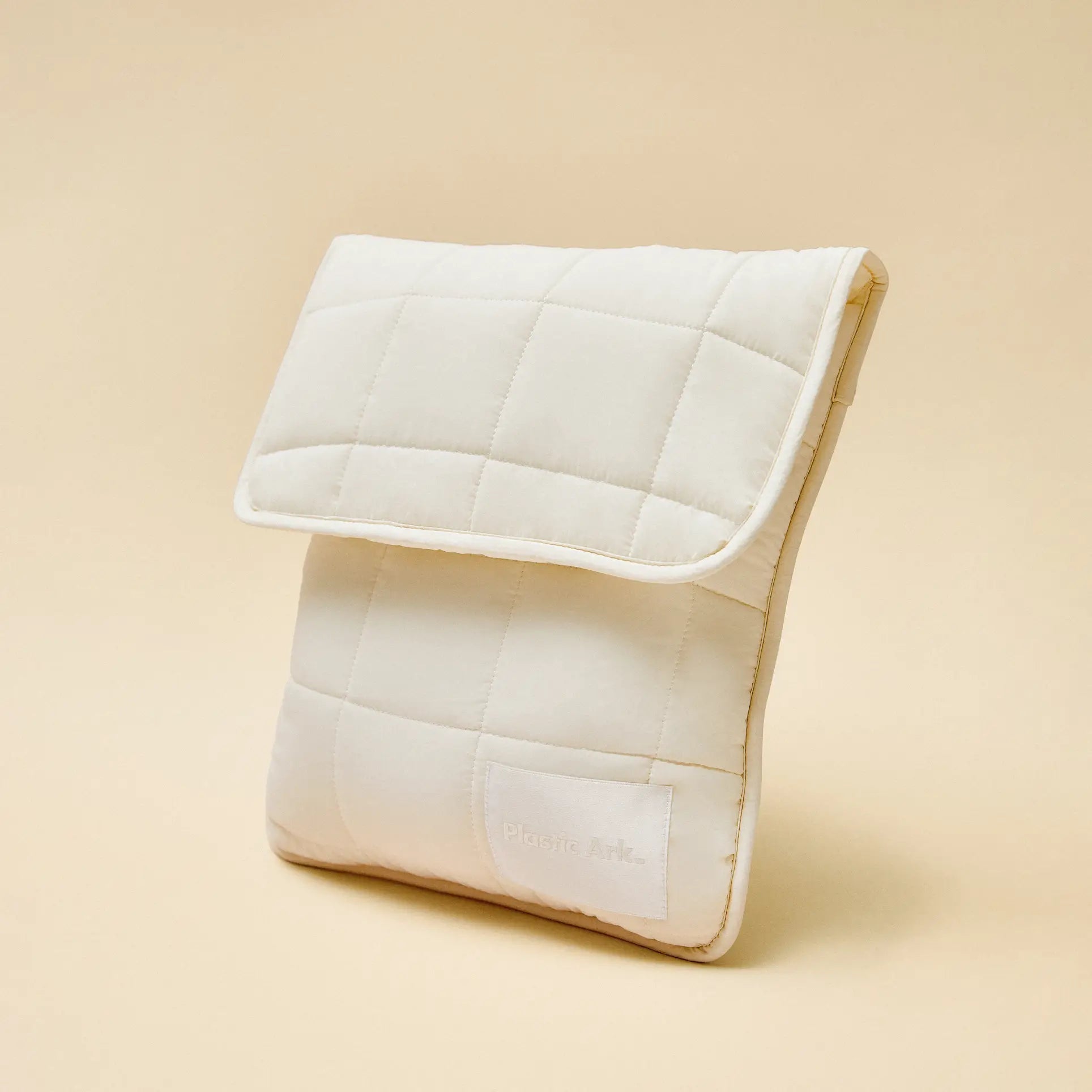 The Plastic Ark Fat Bowl by Plastic Ark is displayed upright against a beige background. Its cream-colored, quilted fabric pouch features a flap closure, minimalist modular design, and a small corner label.