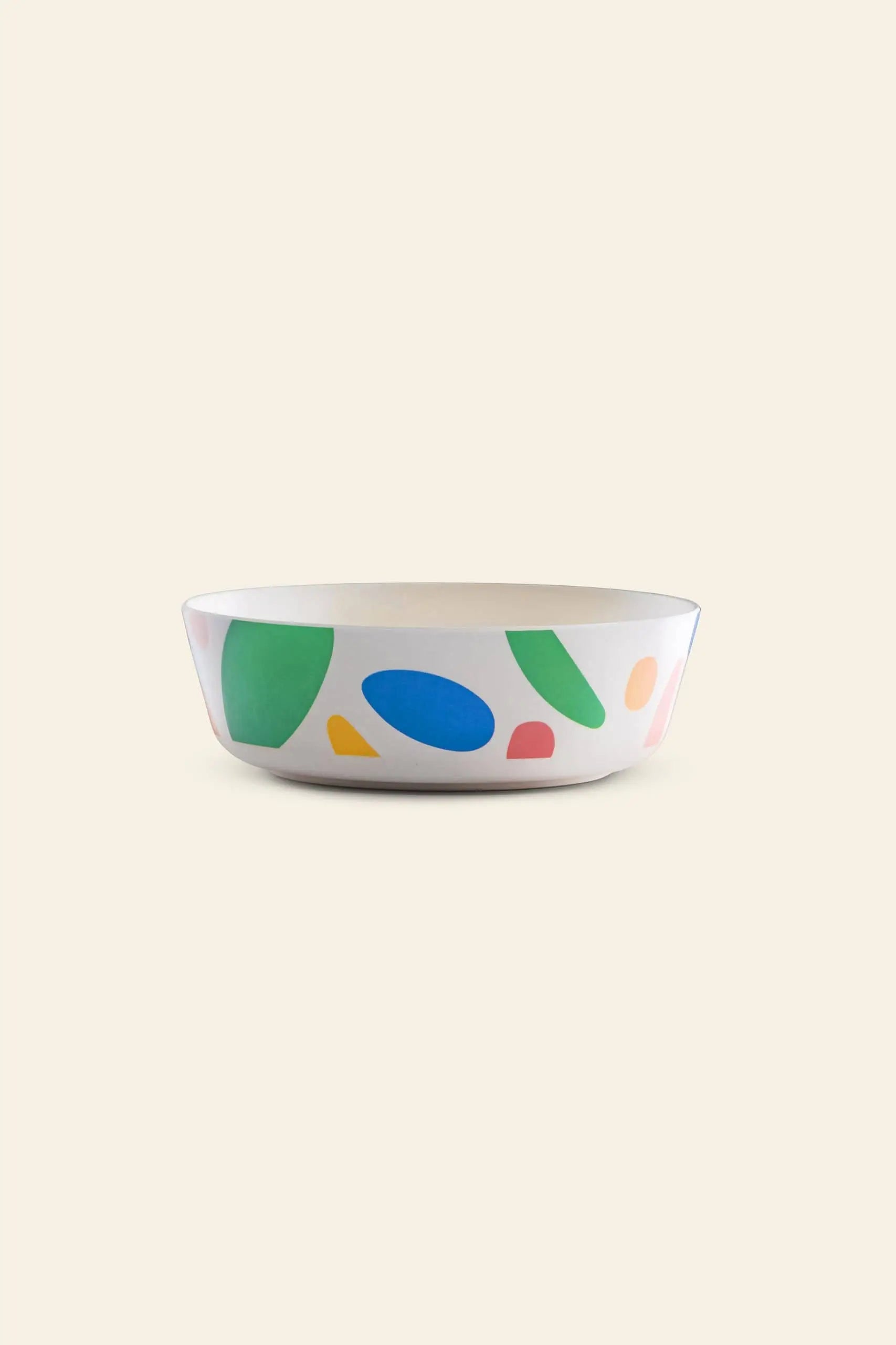 The Poketo Bamboo Bowl by Poketo features colorful abstract shapes in green, blue, pink, and yellow around its sides, set against a plain beige background.