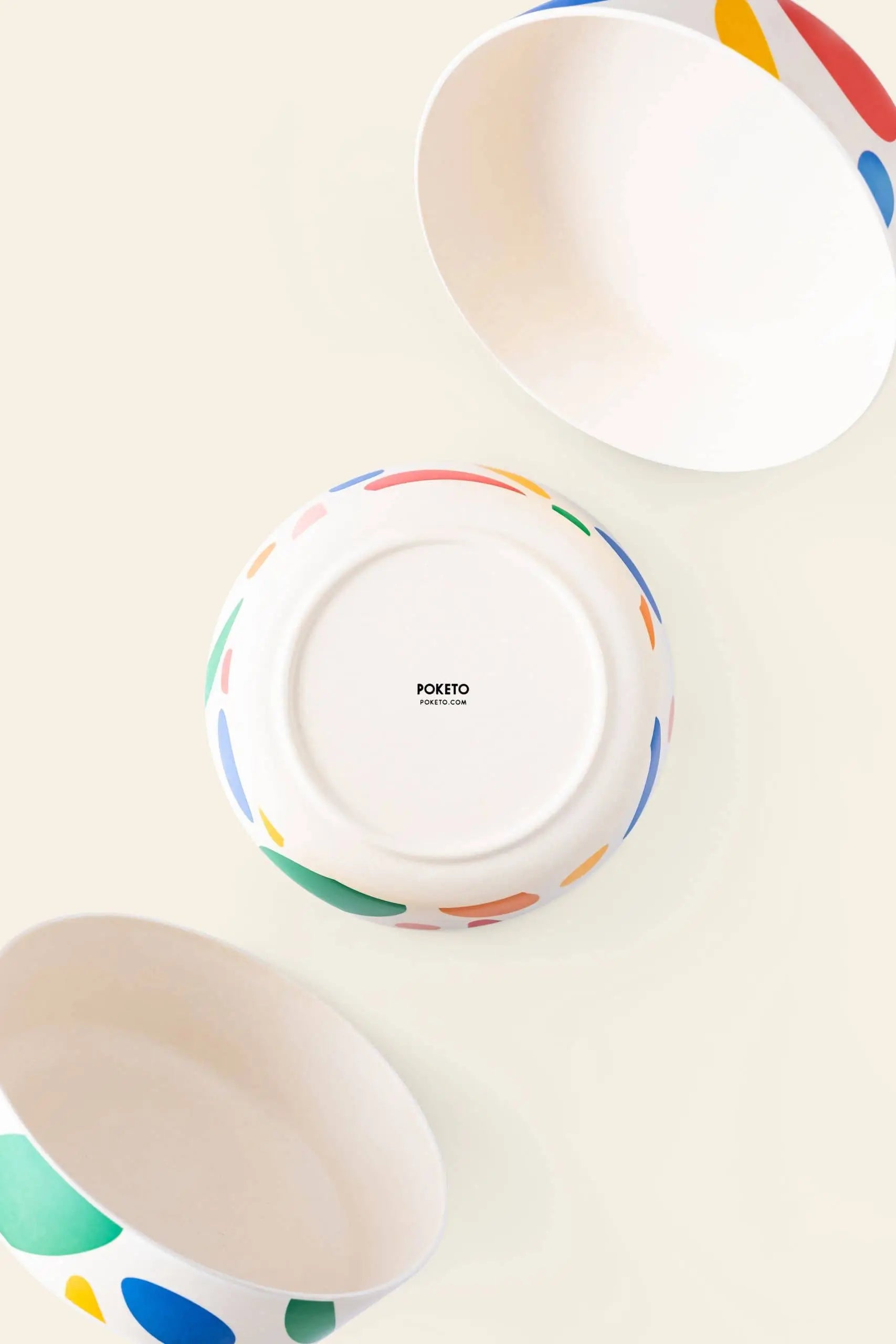 Three Poketo Bamboo Bowls with colorful abstract patterns by Poketo are arranged on a light beige surface; two shown from the side and one upside down, displaying the Poketo logo—ideal for sustainable outdoor dining.
